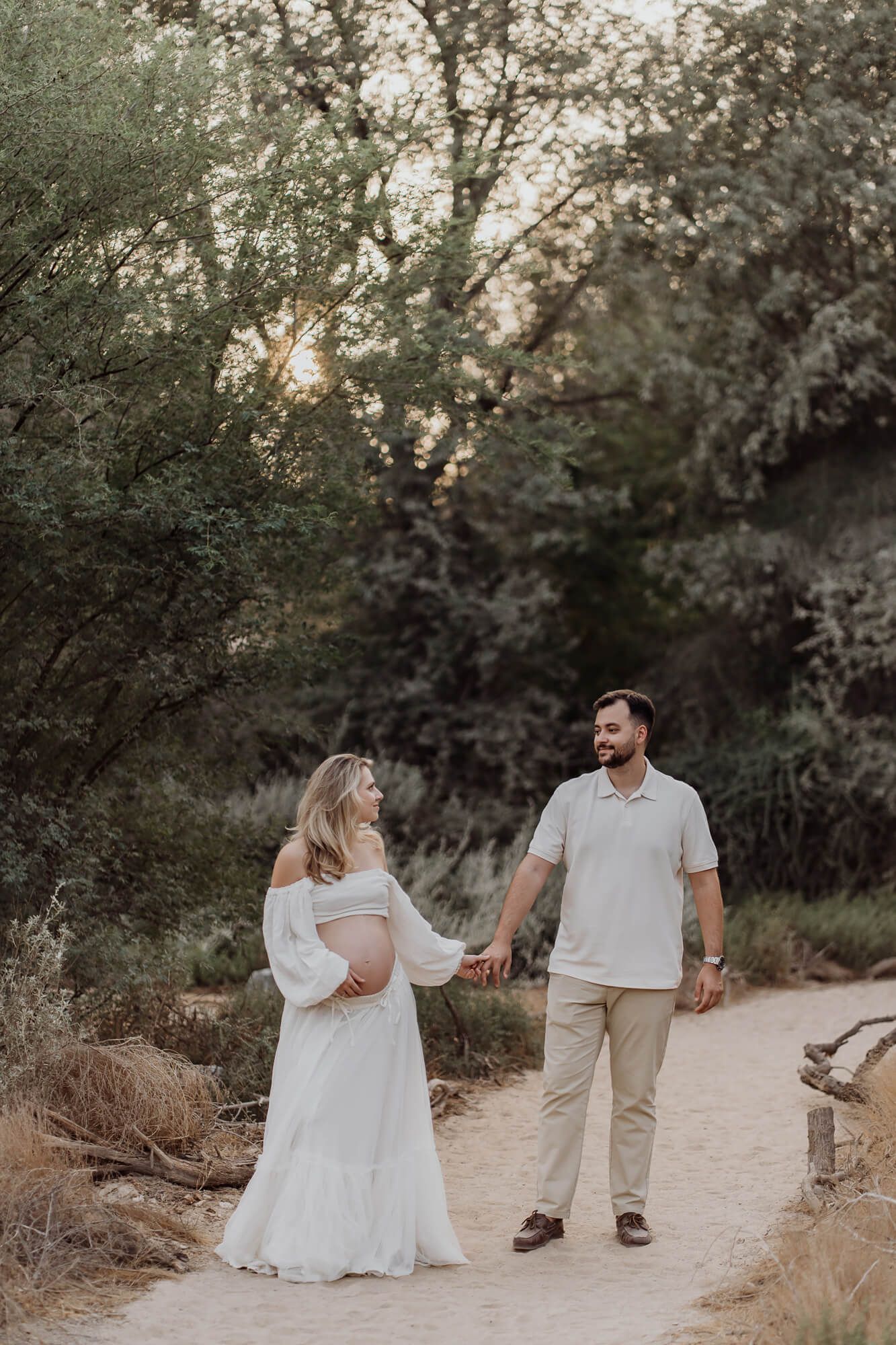 Candid maternity shoot on a desert trail with natural light filtering through trees.