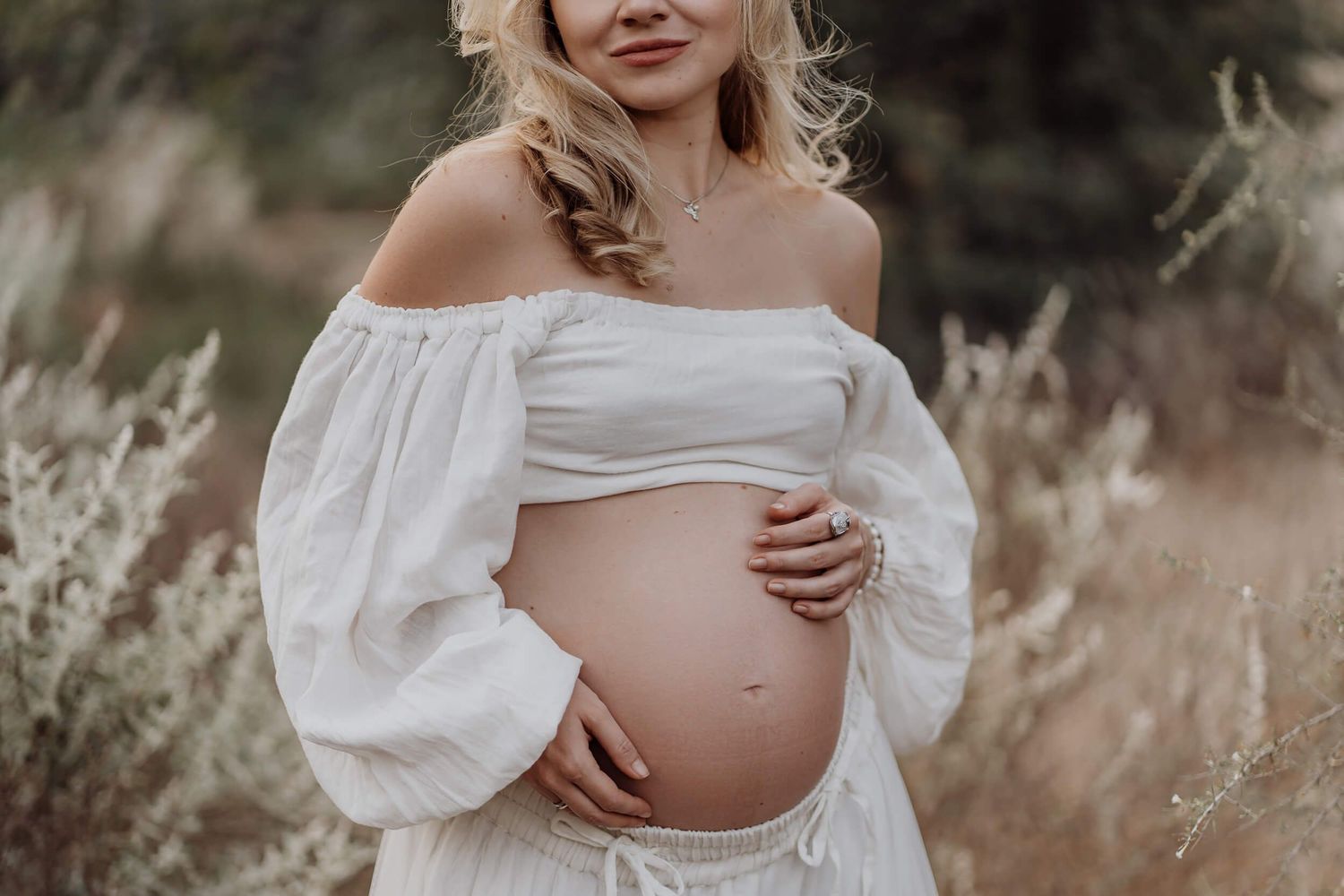 Outdoor maternity photography featuring flowing white dress and natural setting.