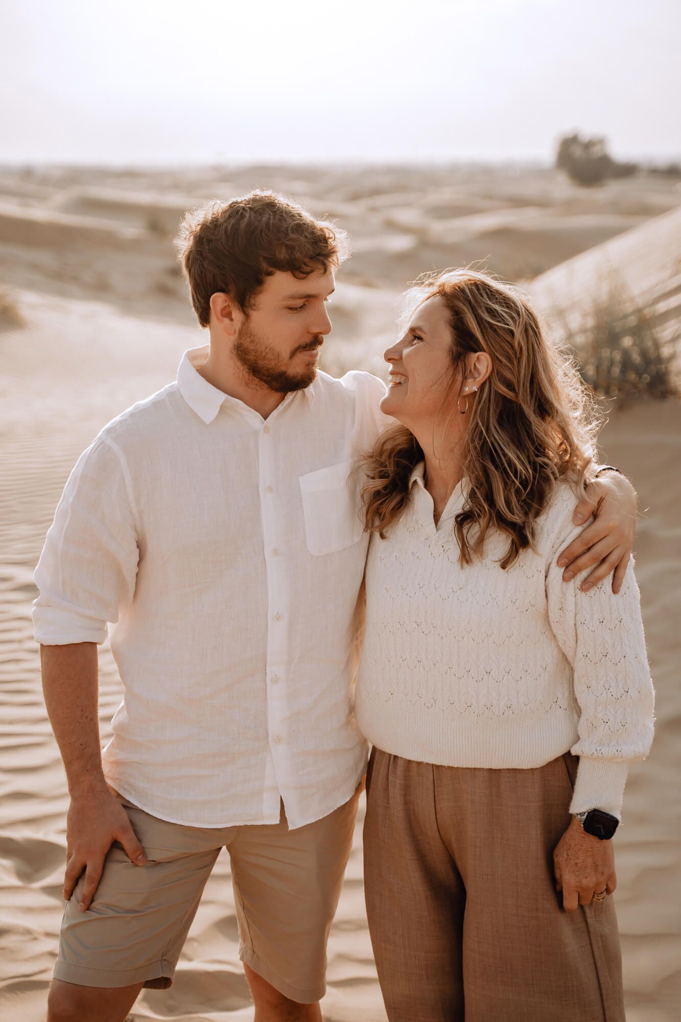 Intimate desert photography with warm lighting and coordinated neutral-colored outfits.