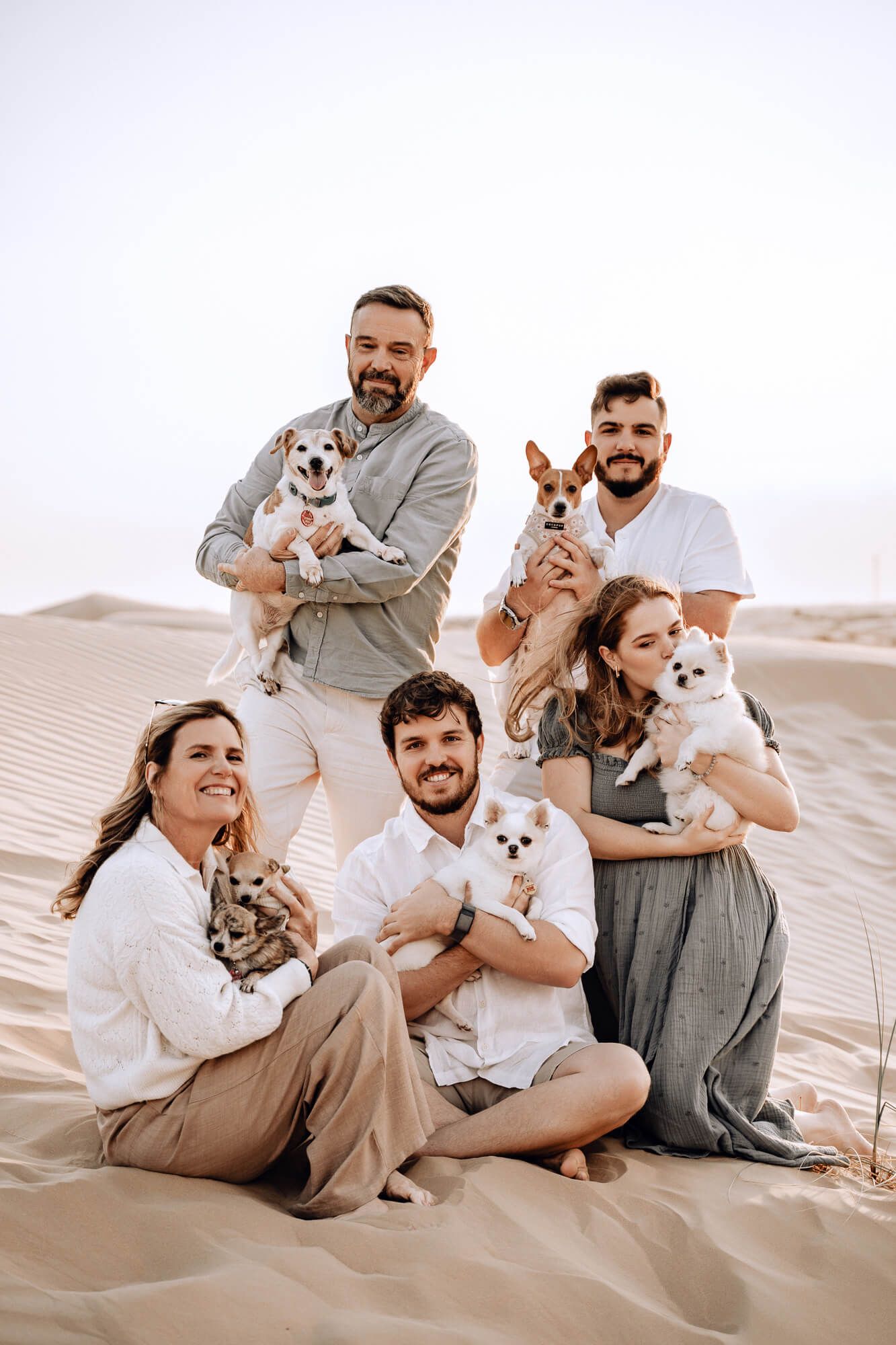 Group photo of five people with their small pets posing together on desert sand.