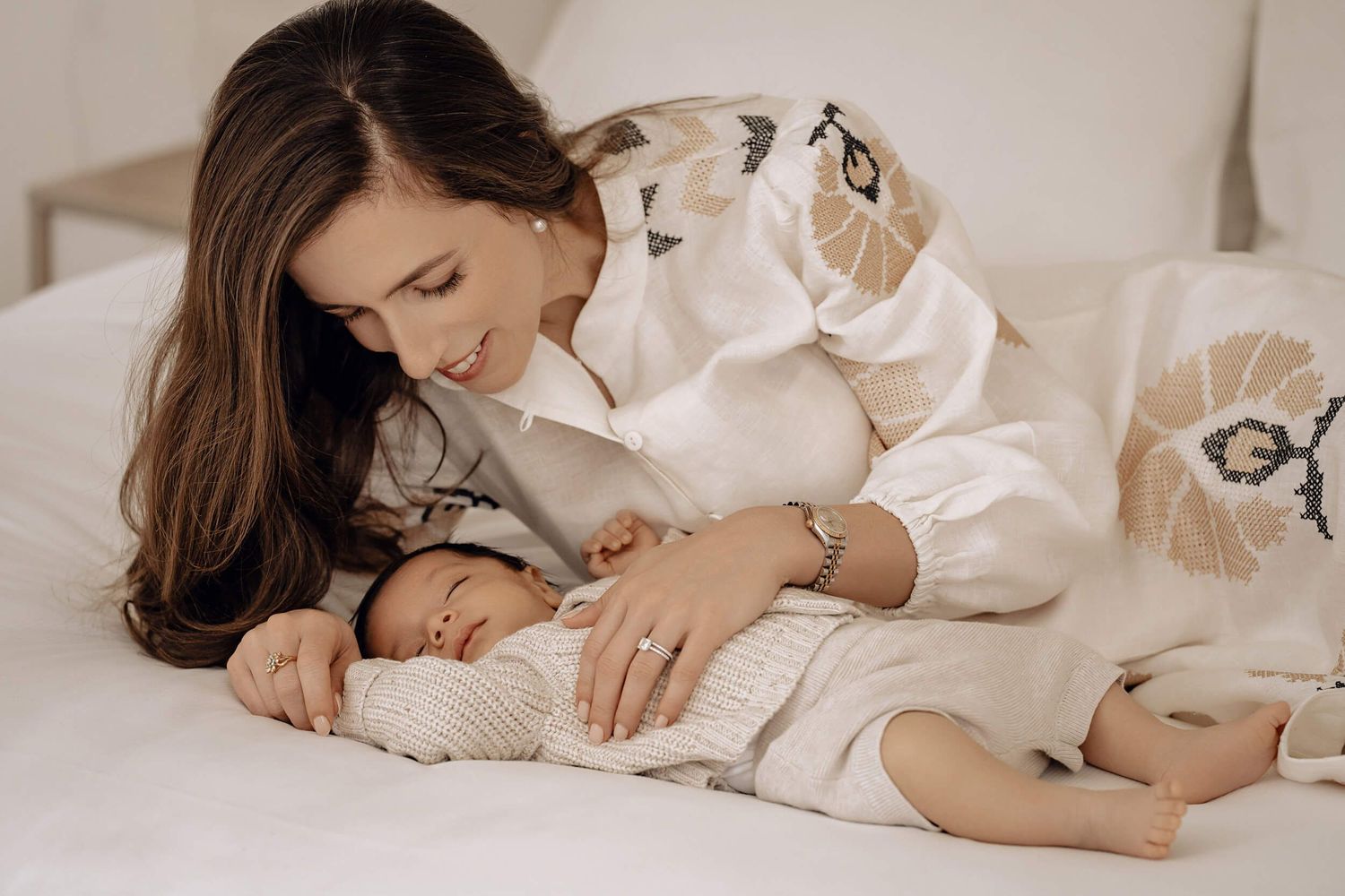 Gentle maternal moment captured on white bedding in soft, warm tones.