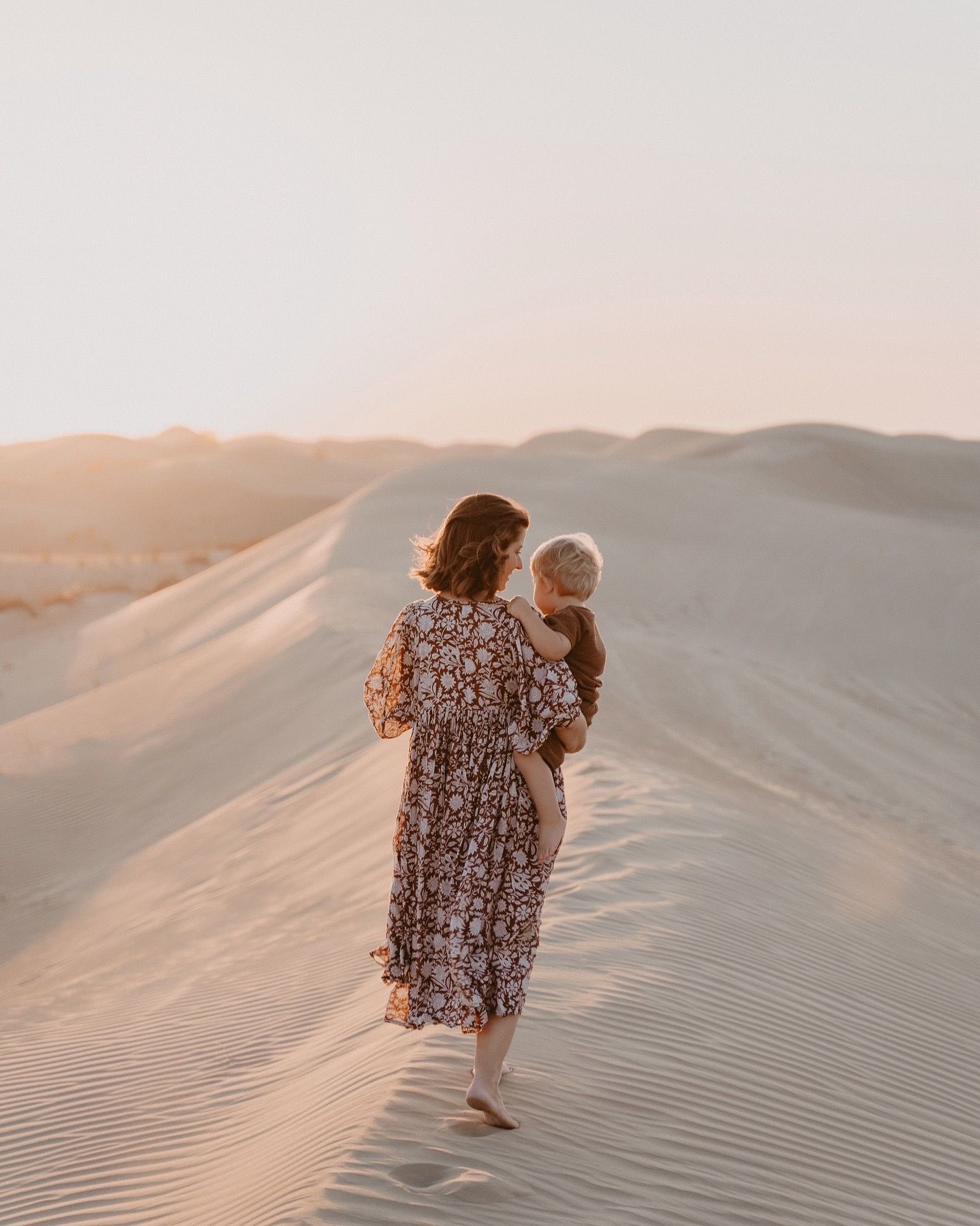 Family walking together up desert sand dunes during golden hour.