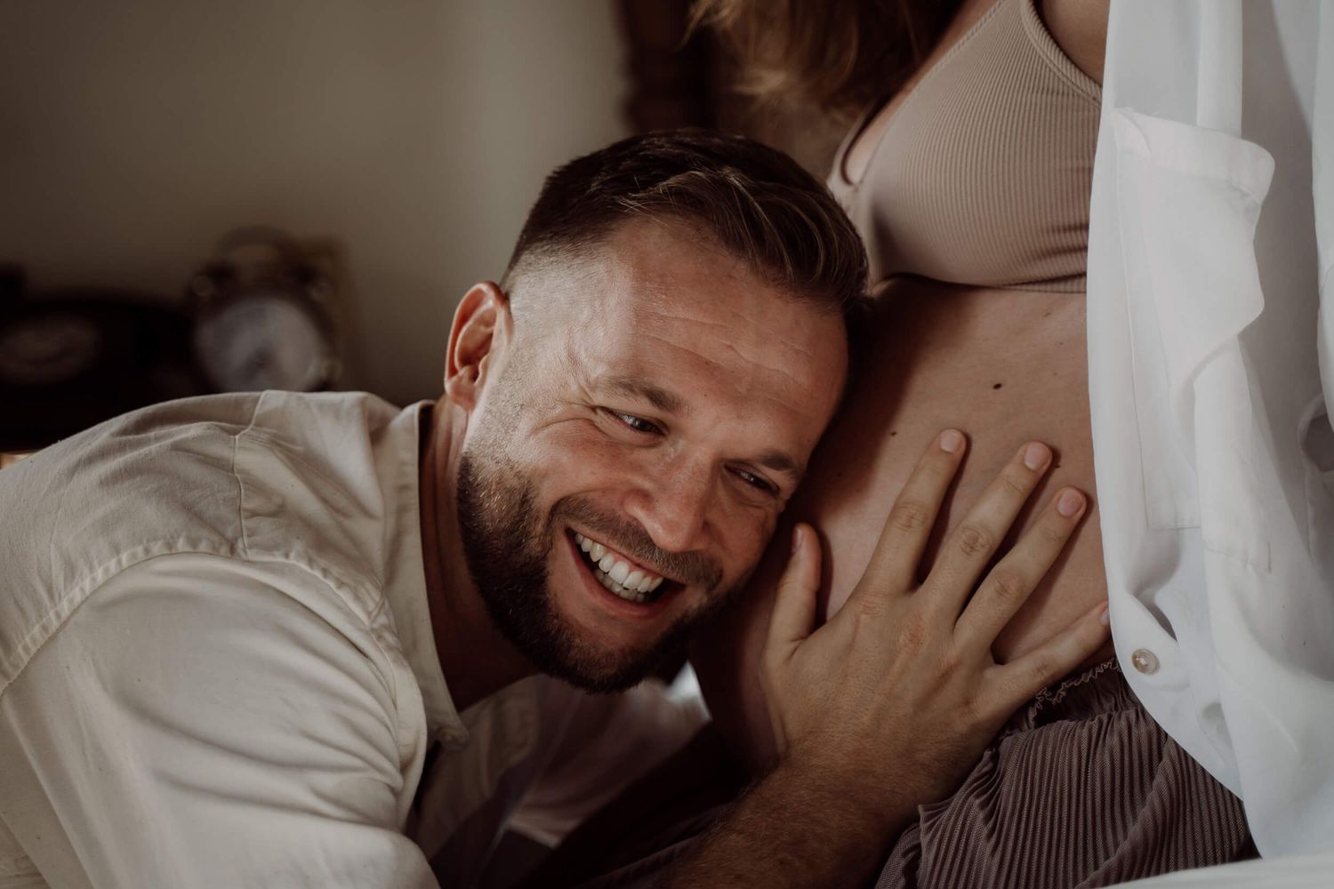 A beaming smile illuminates an intimate maternity moment as a hand gently rests on a pregnant belly.