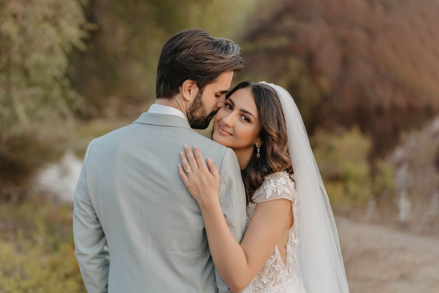 A couple in wedding attire embrace outdoors during a romantic autumn photoshoot with soft natural lighting.