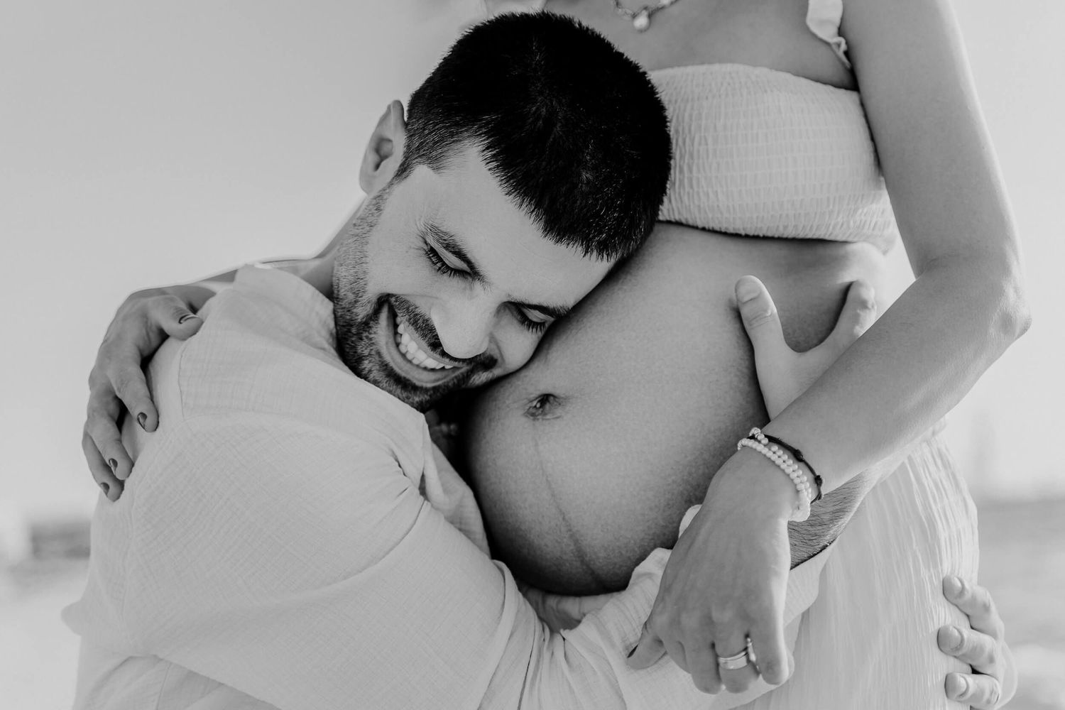 Black and white intimate maternity photo showing tender moment with pregnant belly in soft lighting.