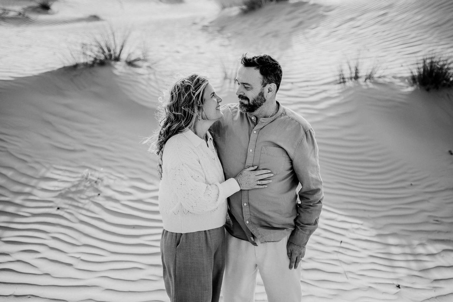 Black and white photo series capturing tender moments between a couple on sand dunes.