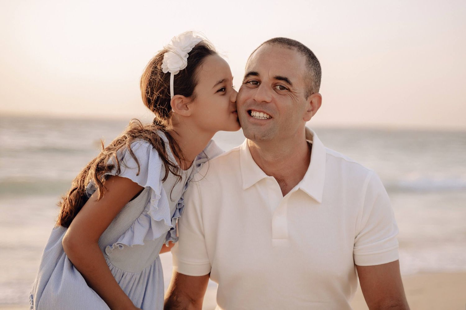 Playful beach portrait session with family members in coordinated white and neutral attire.