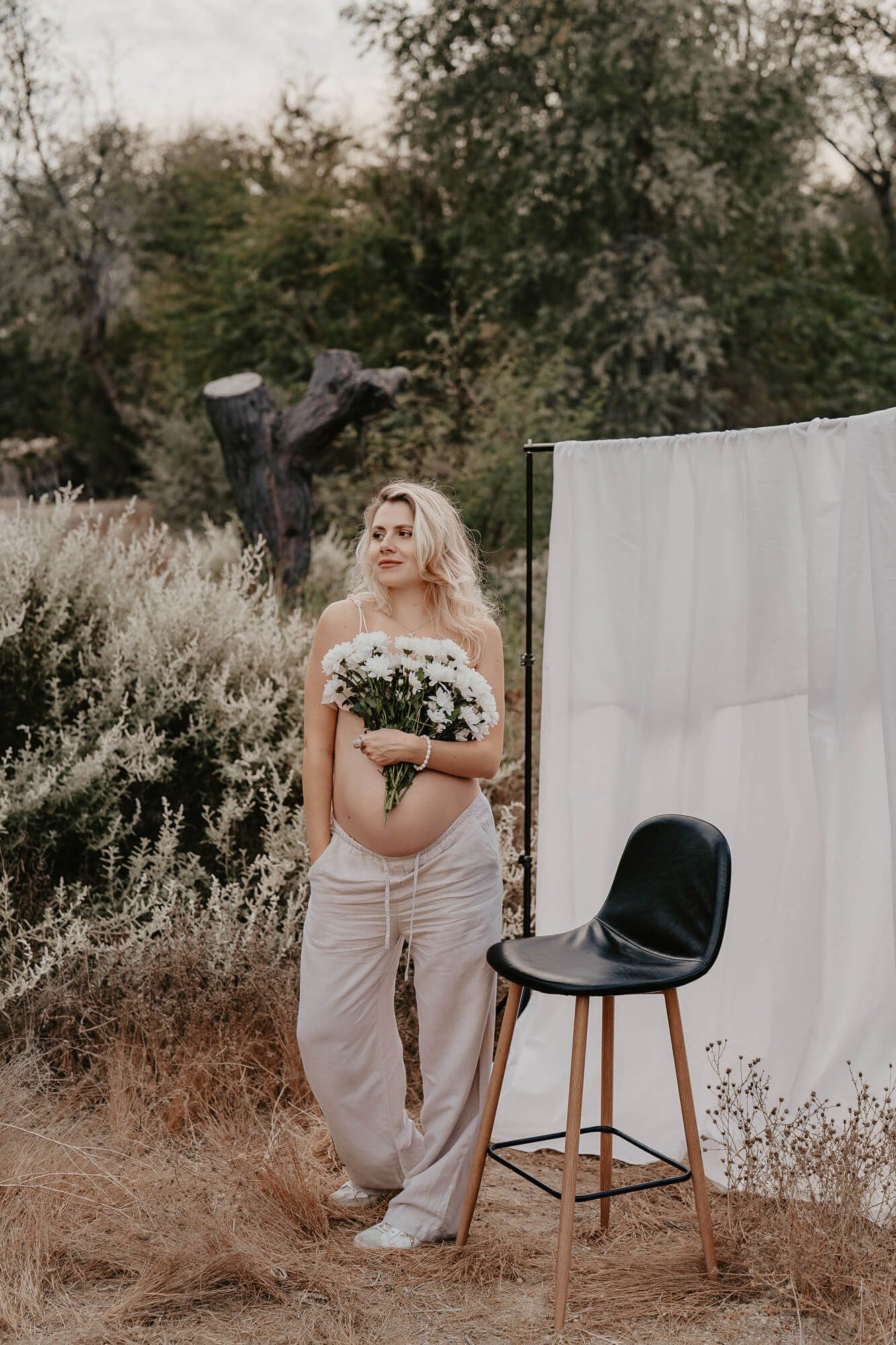 Rustic outdoor photo session with white backdrop and vintage chair in tall grass.
