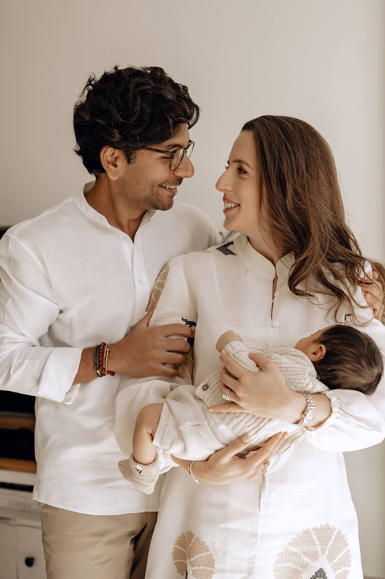 Family portrait with new parents in white clothing sharing joyful moment with baby.