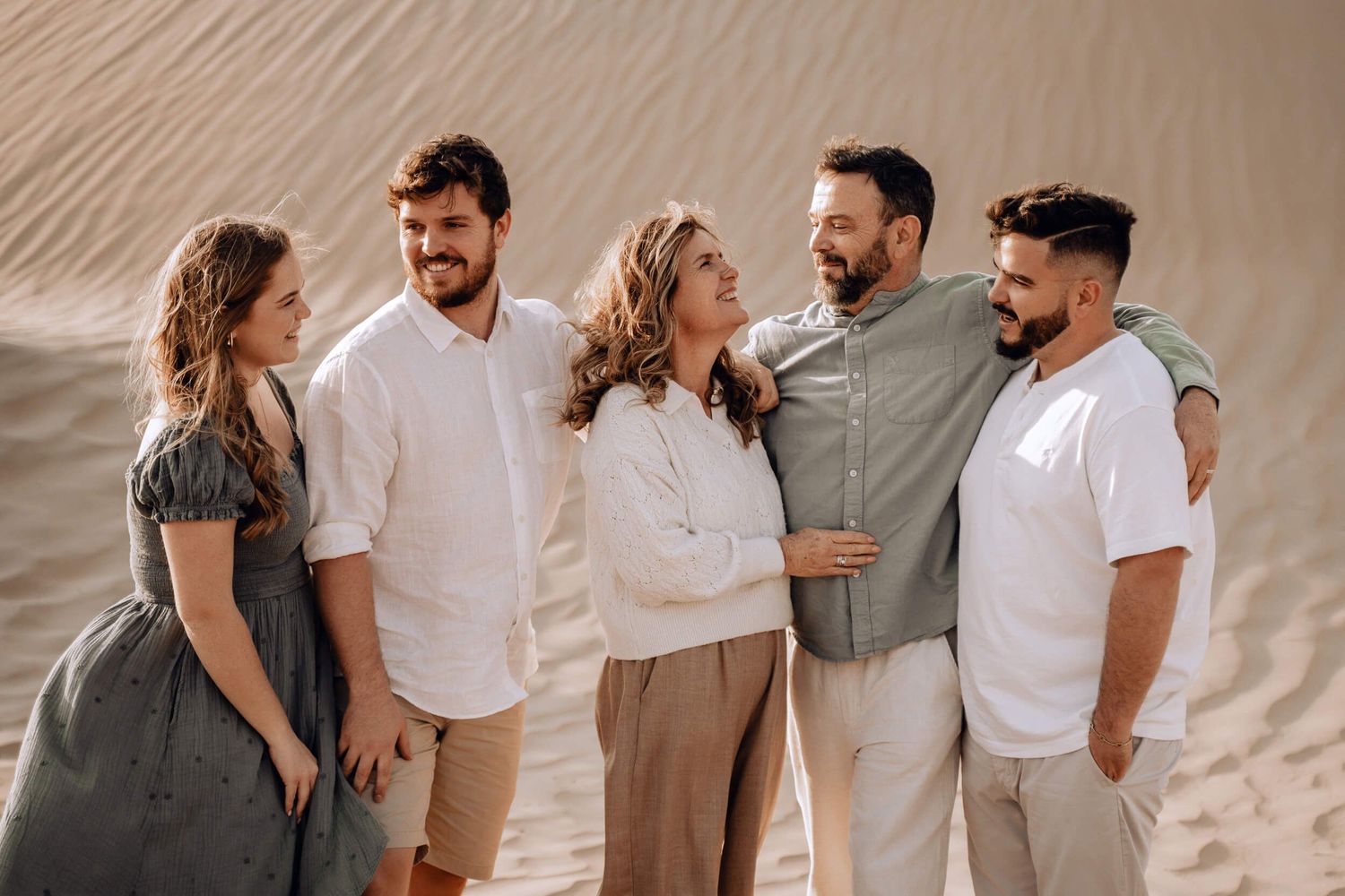 Candid moment of five people laughing together during desert photo shoot in coordinated outfits.