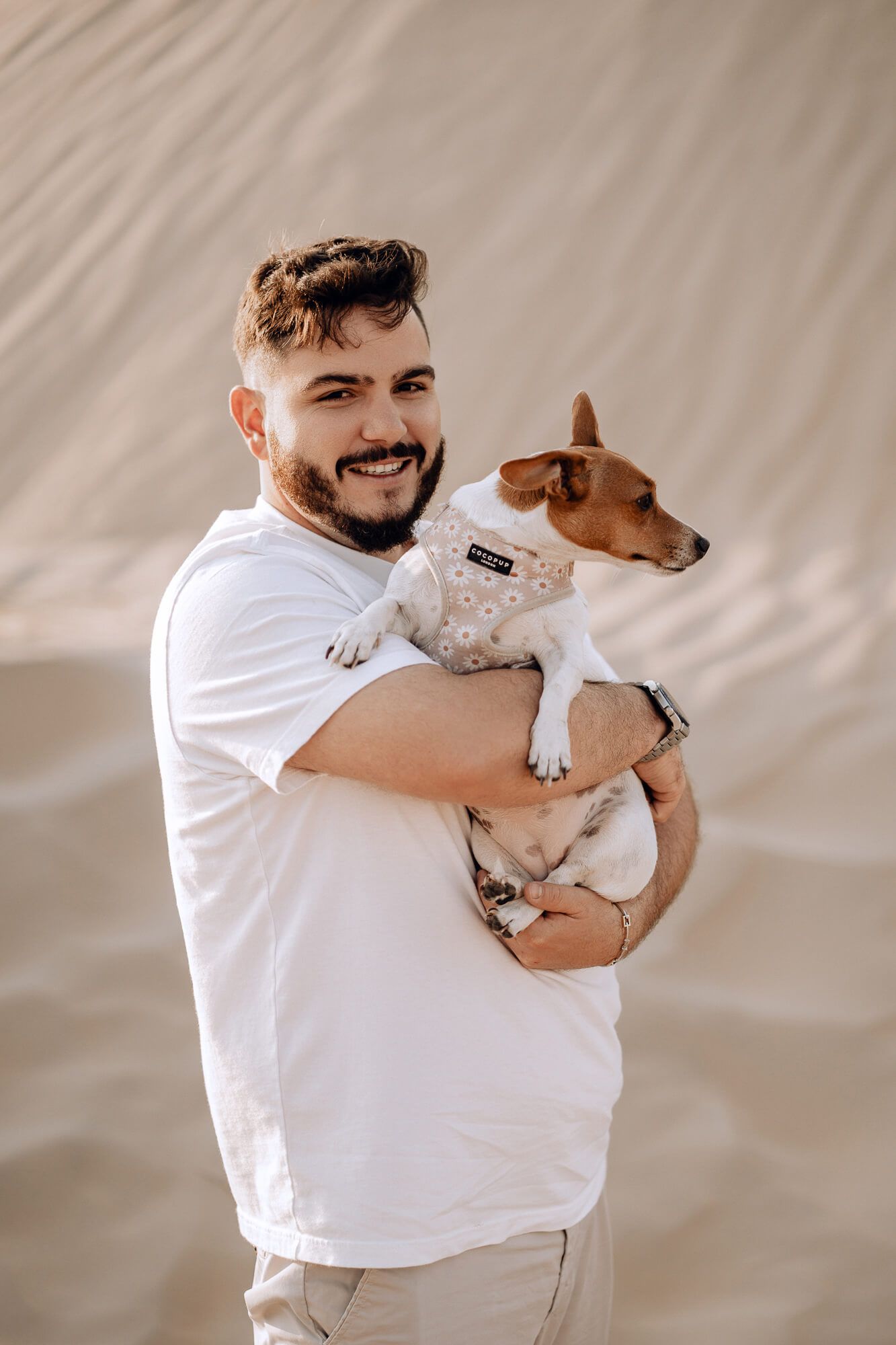 Person in white shirt holding small brown and white dog against desert backdrop.