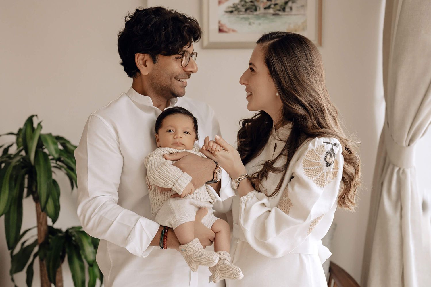 Happy family moment captured indoors with parents in white clothing holding their infant.