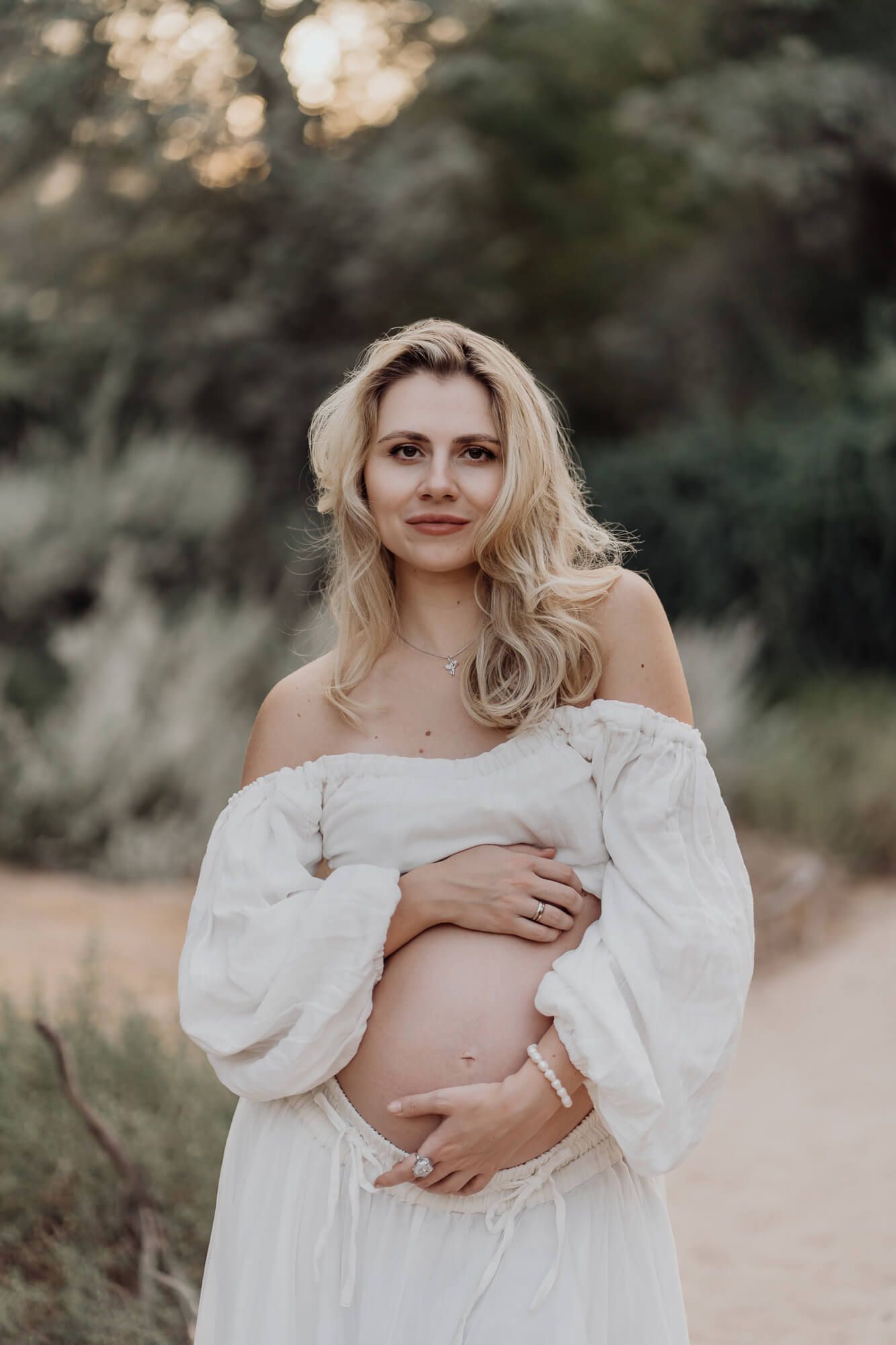 A serene outdoor maternity session with a white flowy dress against a natural backdrop.