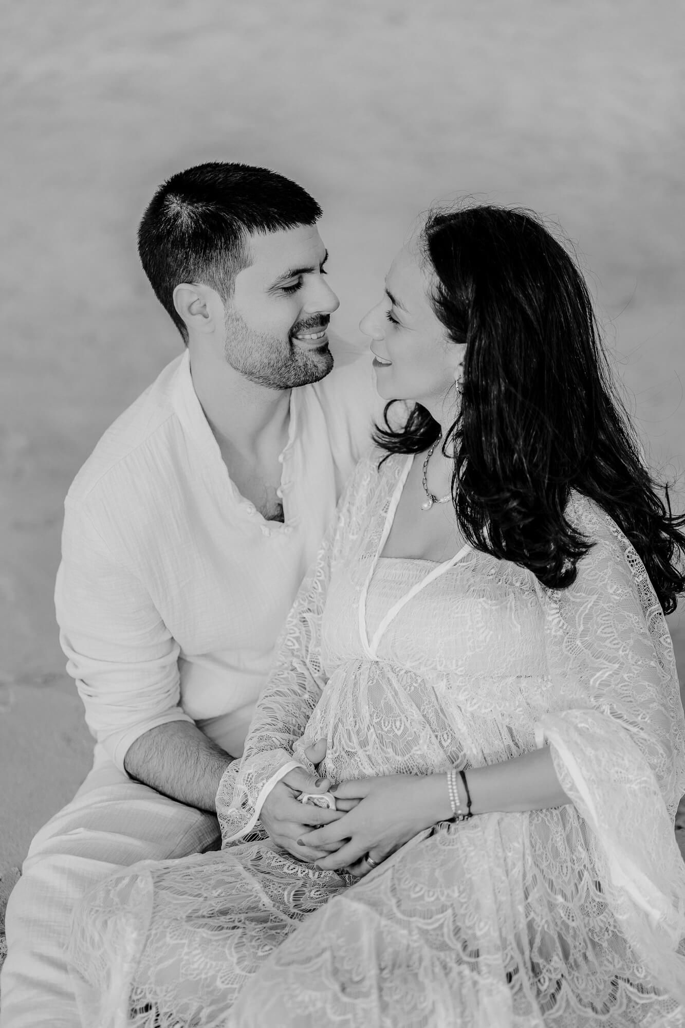 A romantic black and white portrait of a couple in white outfits sharing an intimate moment together.