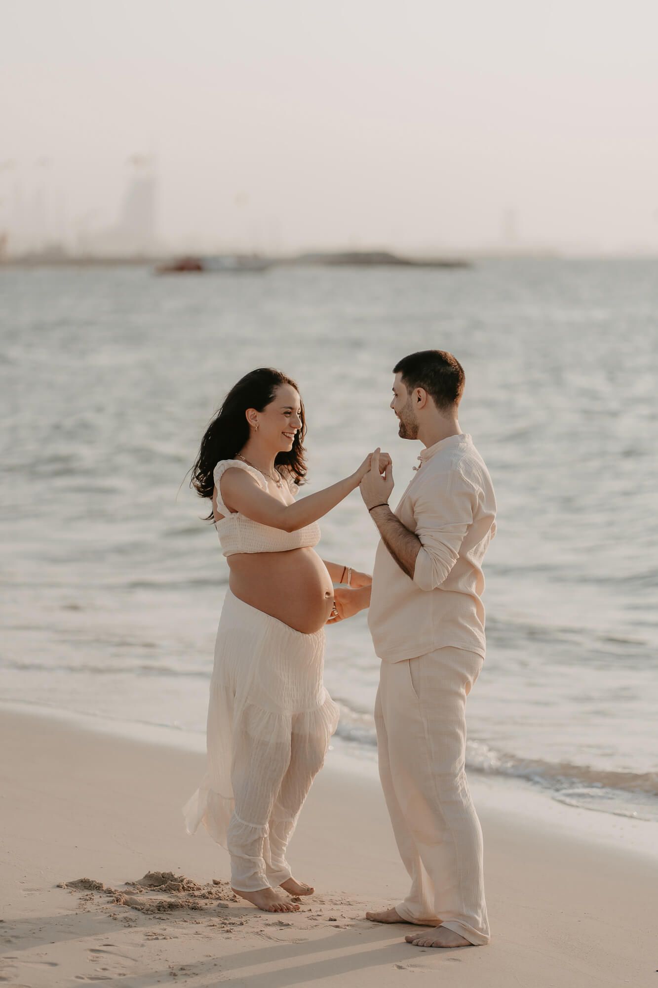 Expecting couple shares a joyful moment together on a misty beach at sunset.