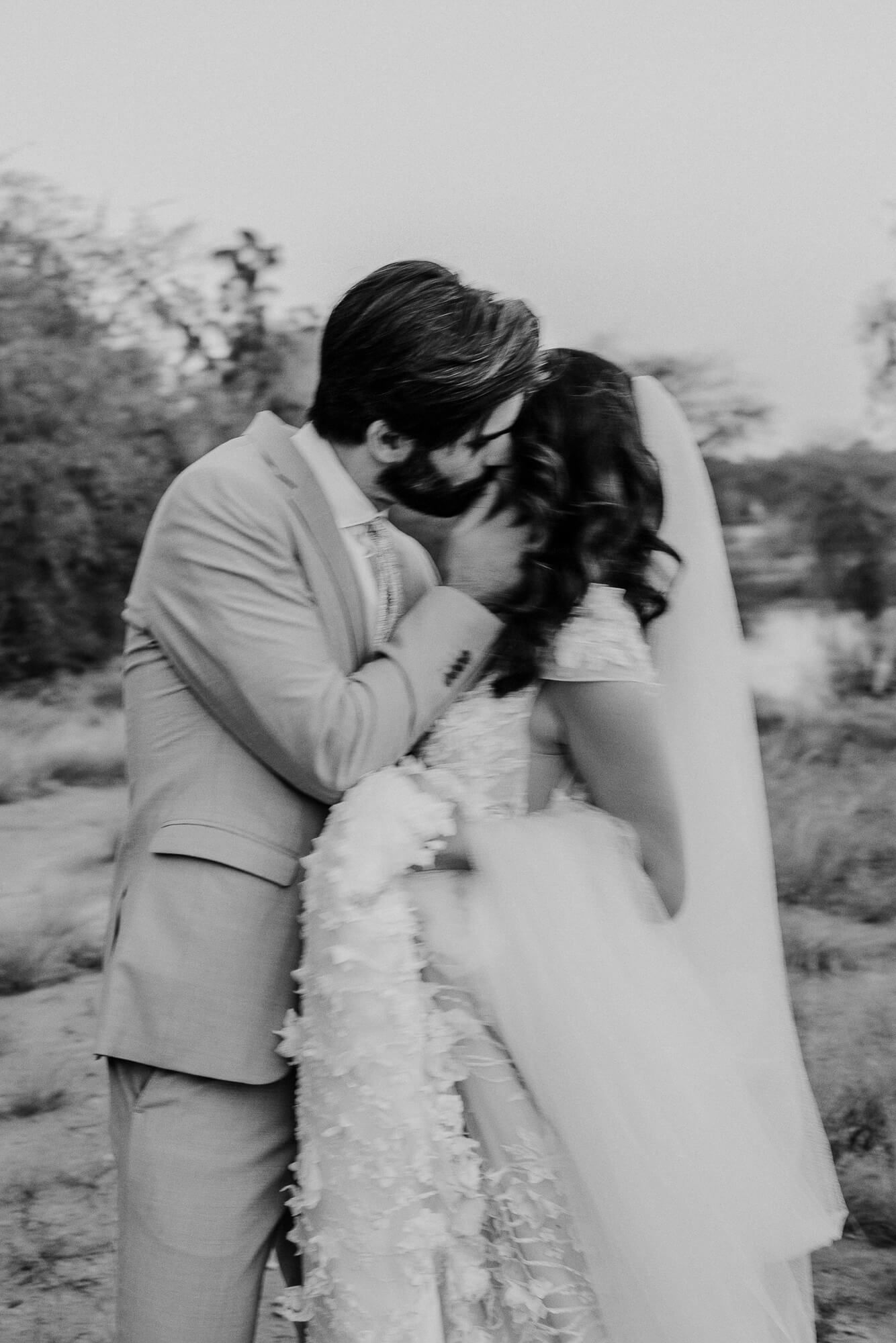 A romantic black and white wedding photo showing a tender moment between newlyweds in an outdoor desert setting.