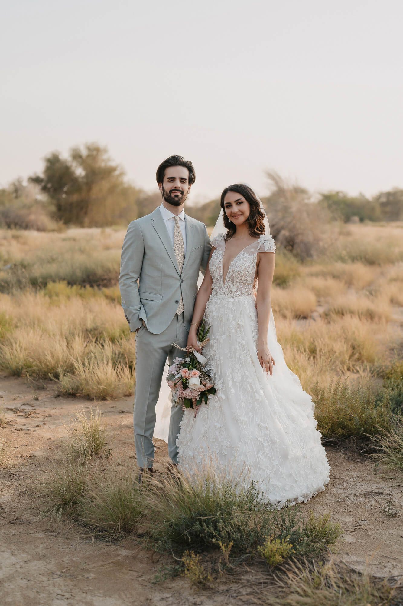 Newlywed couple poses together in natural desert landscape during golden hour wedding photoshoot.
