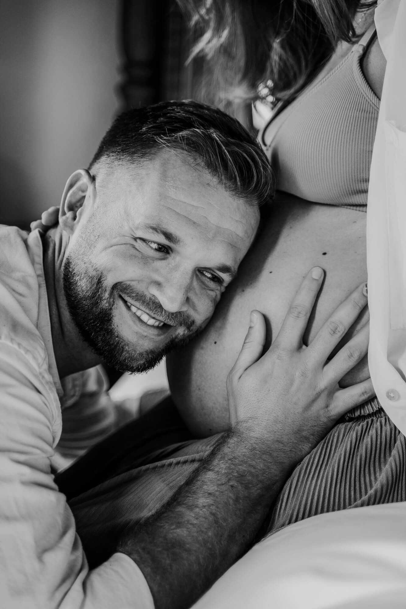 Intimate black and white photo of an expectant couple sharing a tender moment with hands on pregnant belly.