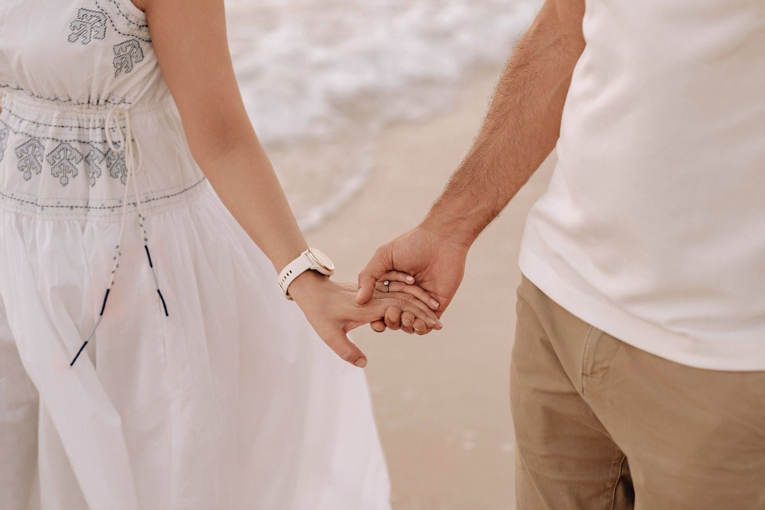 Close-up of couple's hands clasped together while walking on beach.