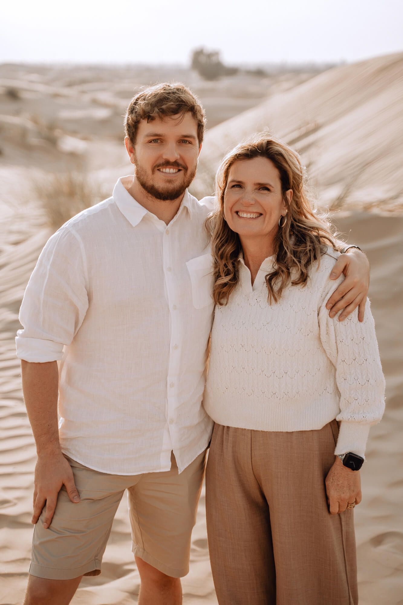 Mother and son in desert sand dunes with coordinated neutral outfits creating a warm sepia-toned atmosphere.