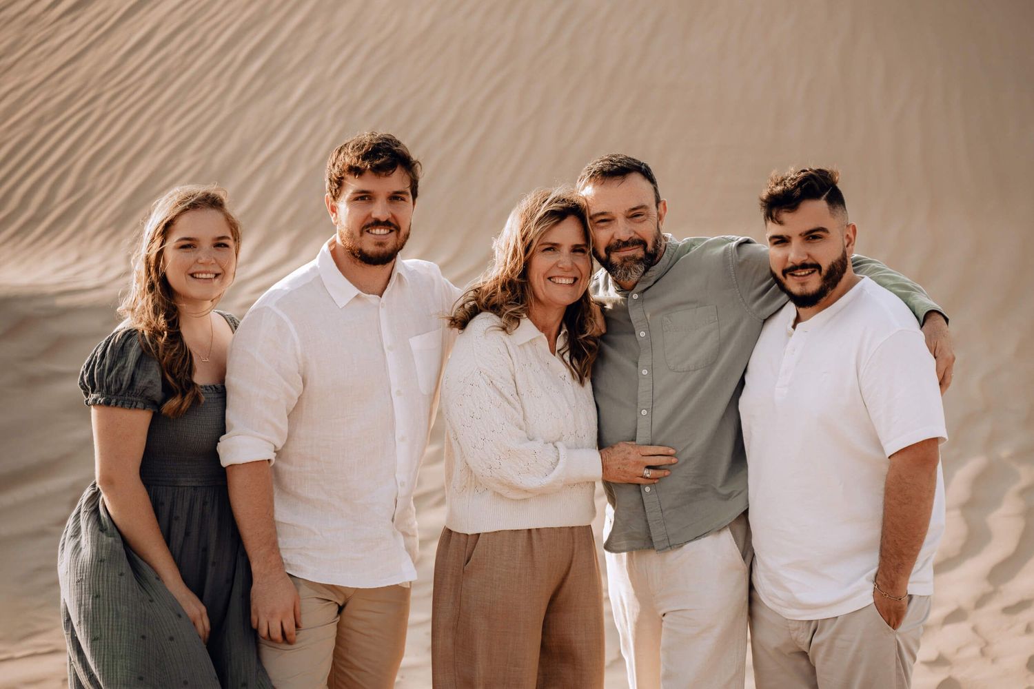 Close-up group portrait of five people in light colored clothing against textured sand dune background.