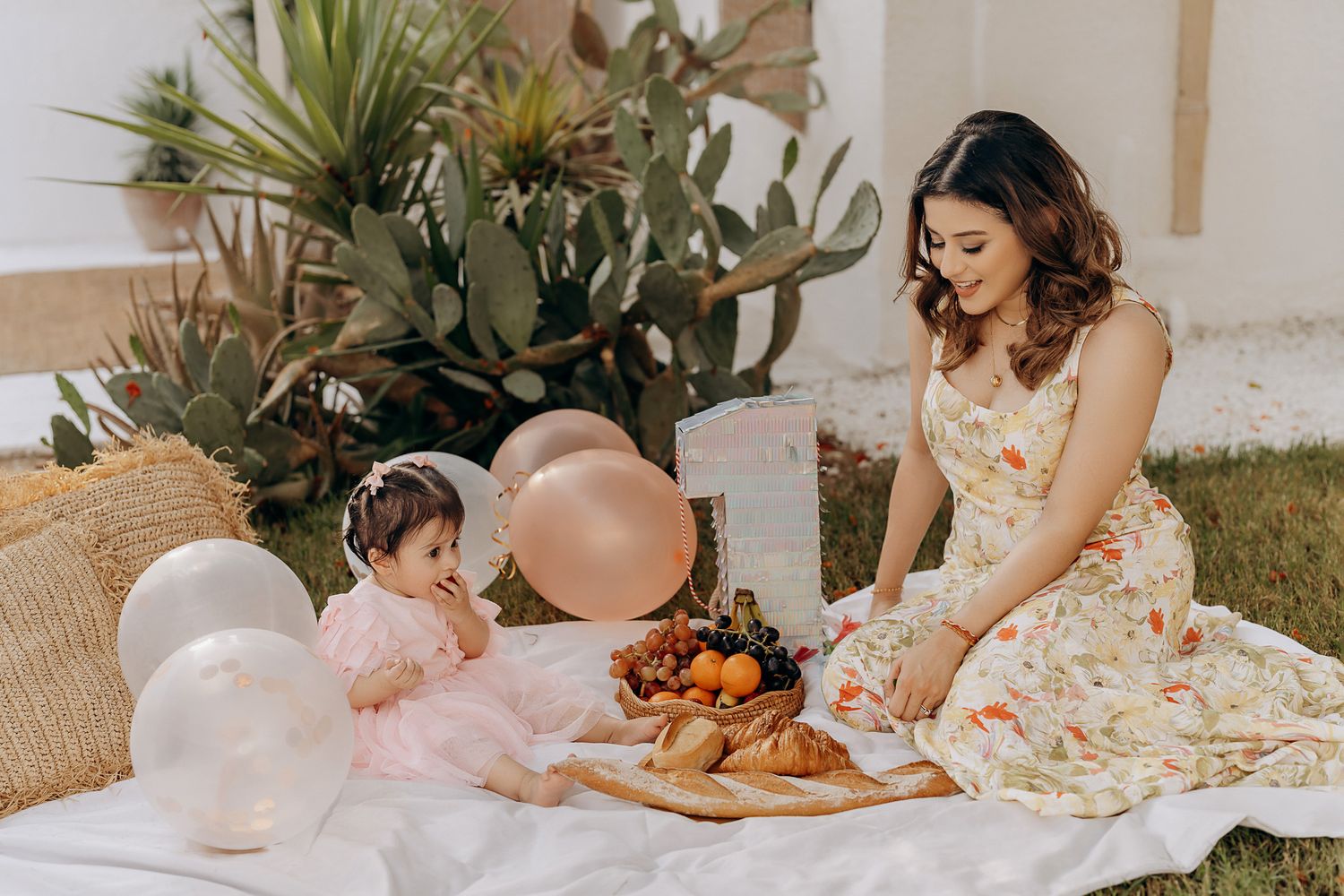 An outdoor picnic setup with white balloons, pastries, and tropical plants in a garden setting.