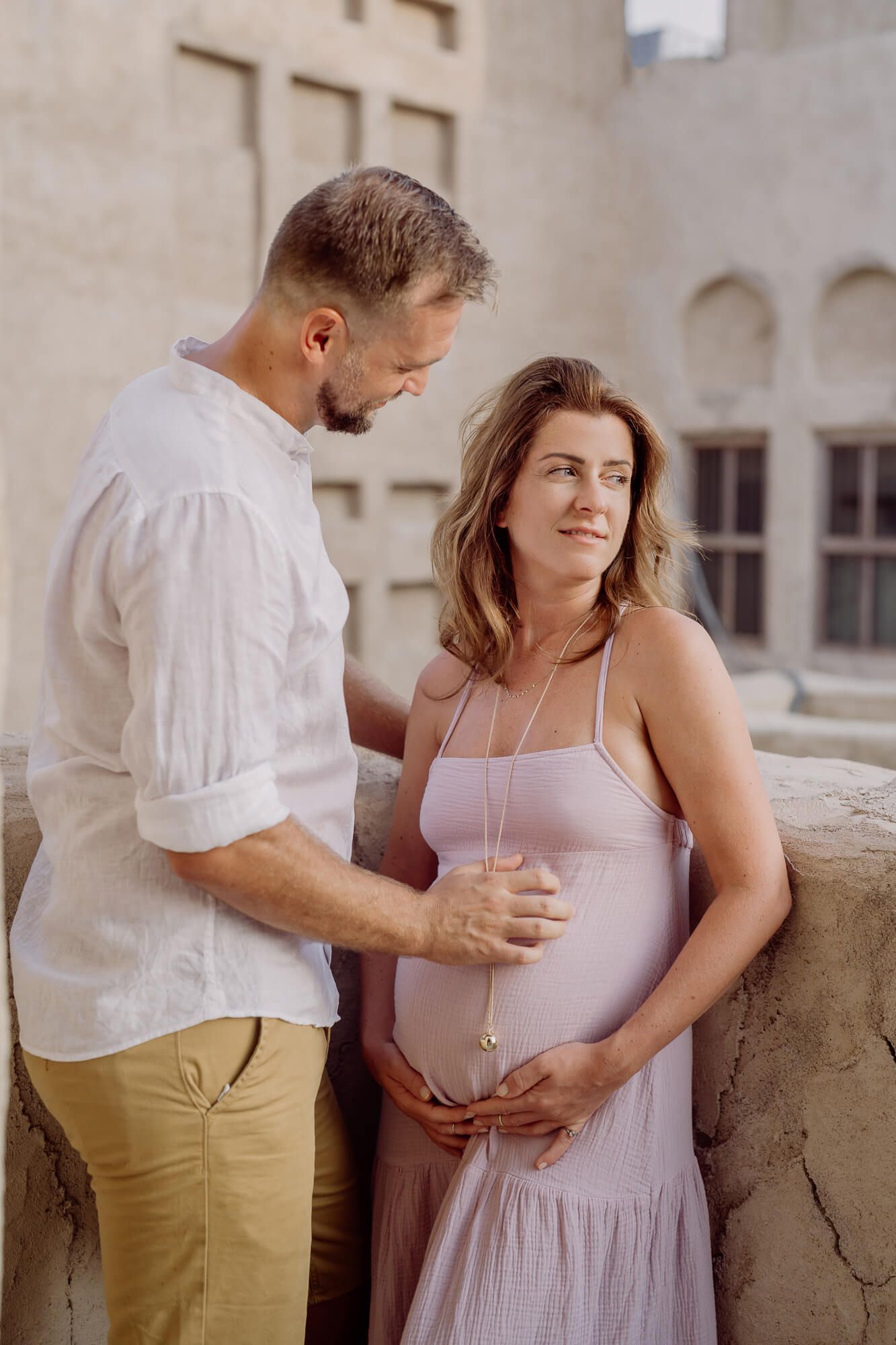 Romantic pregnancy portrait showcasing a couple in casual attire against a traditional architectural backdrop.