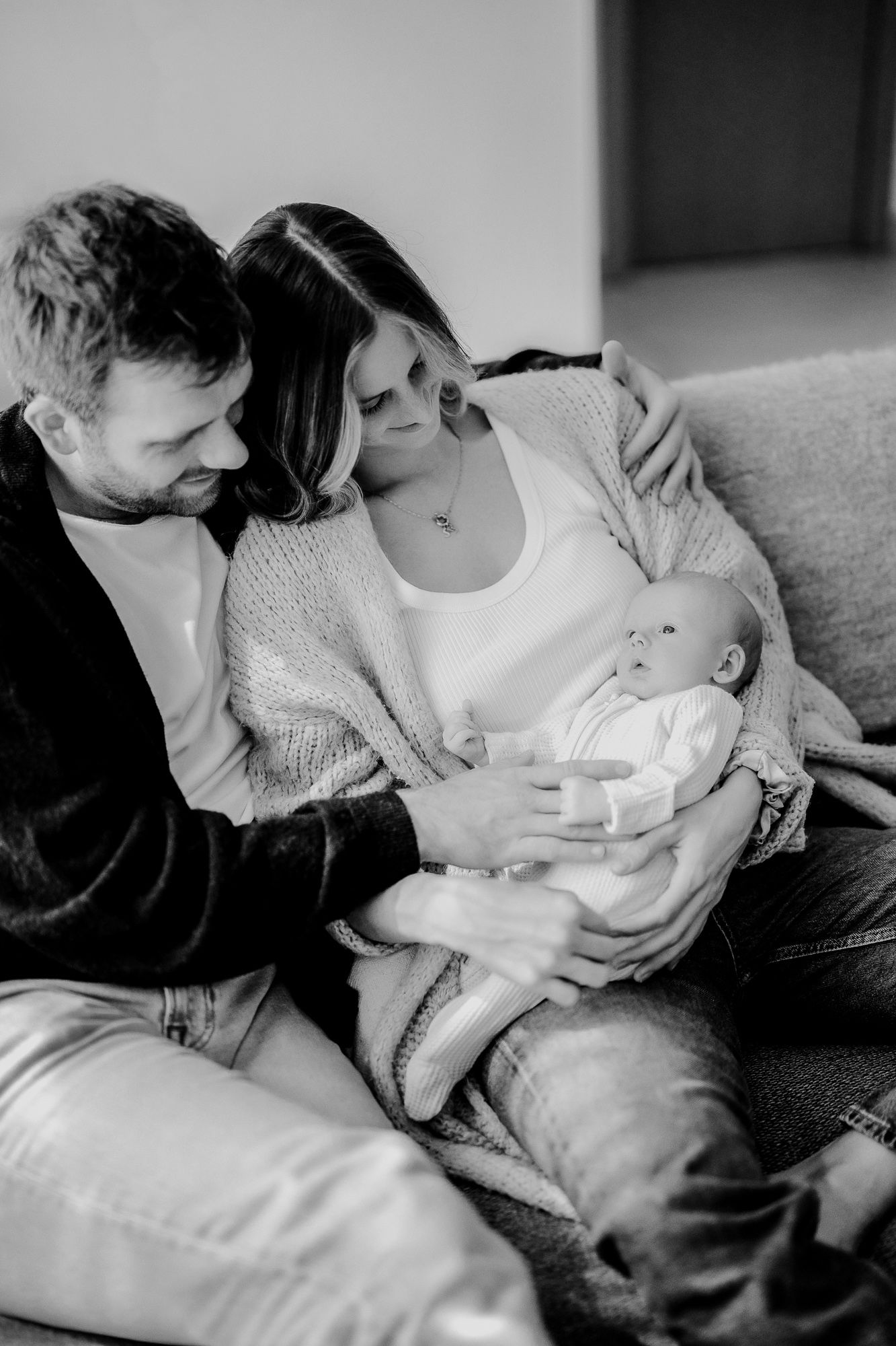 Black and white tender moment between parent and newborn baby sleeping peacefully on a couch at home.