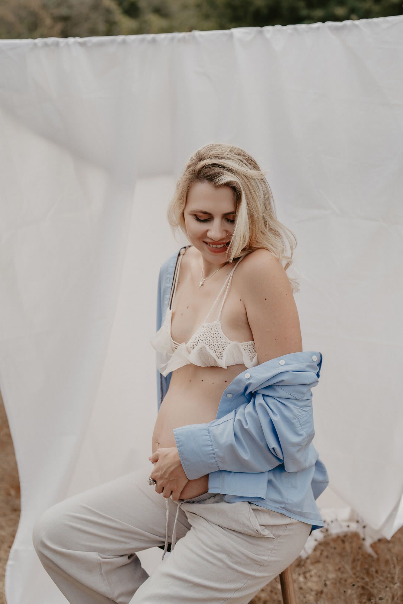 Maternity boudoir photo against white backdrop featuring soft blue denim shirt and cream lingerie.