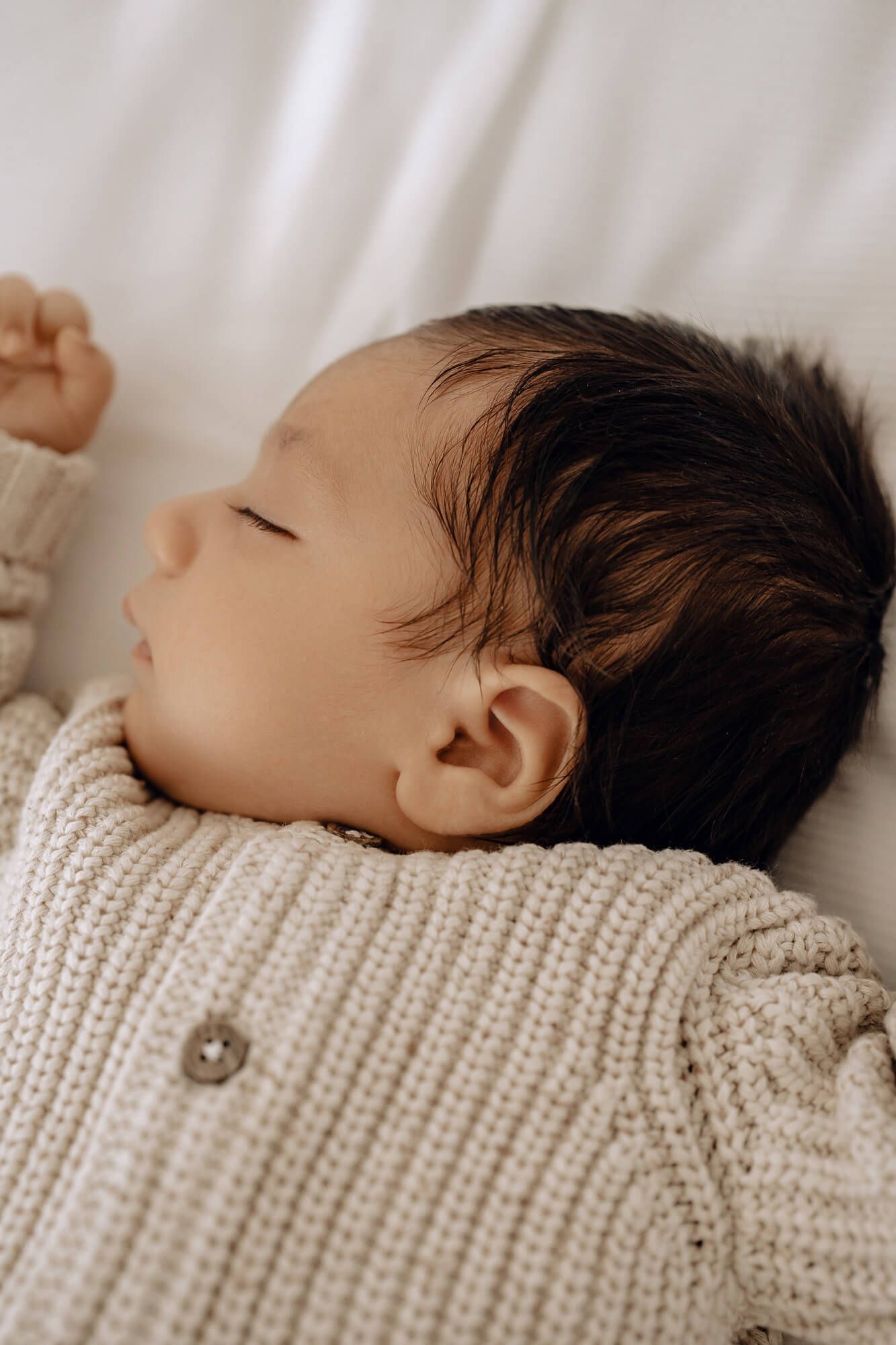 Close-up of peaceful baby resting in cozy white knit sweater on soft bedding.