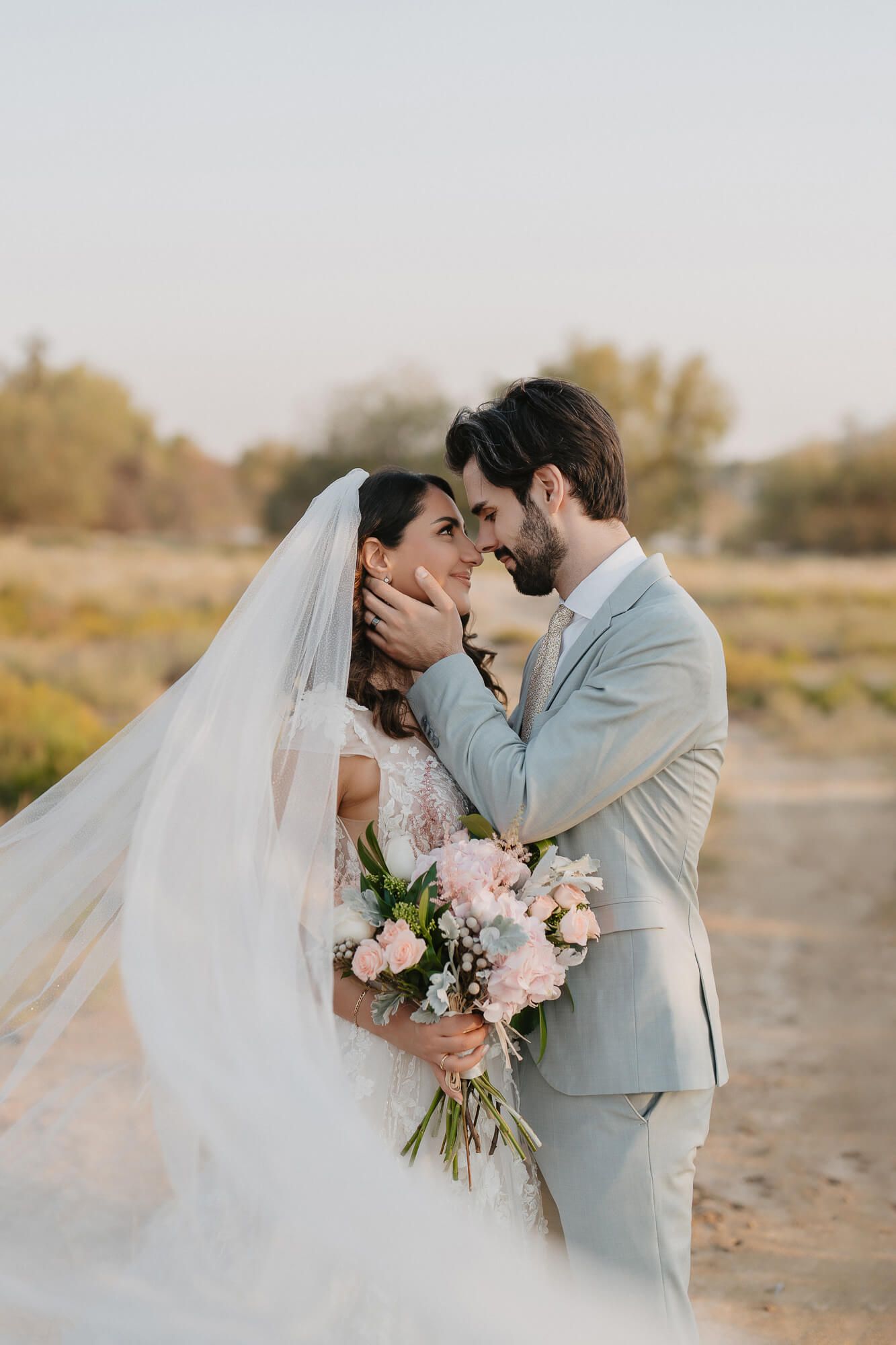 Romantic wedding couple embraces outdoors with pink bouquet during golden hour sunset in autumn field.