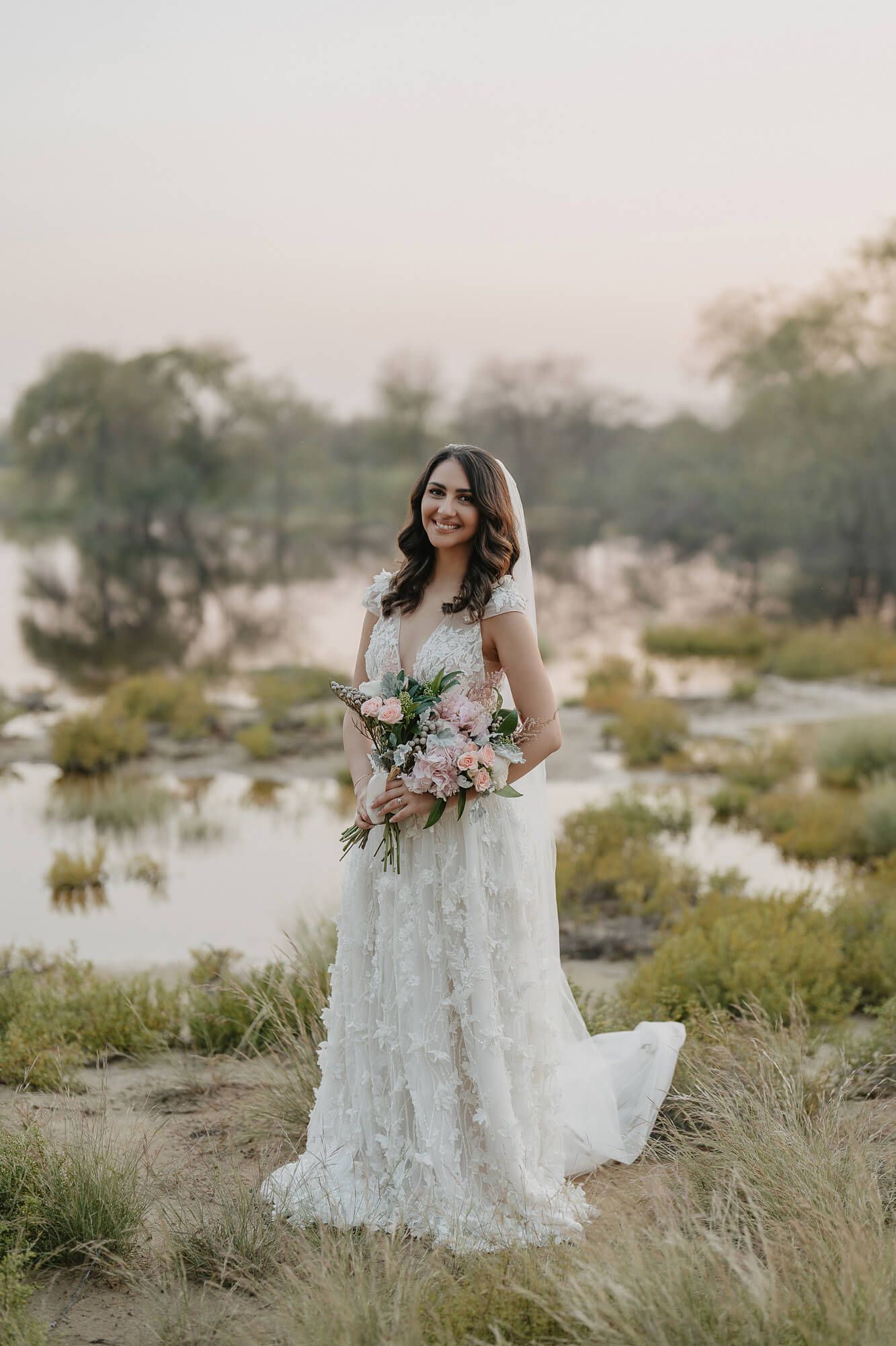 A romantic bridal portrait series taken in a natural setting with tall grass and water at golden hour.