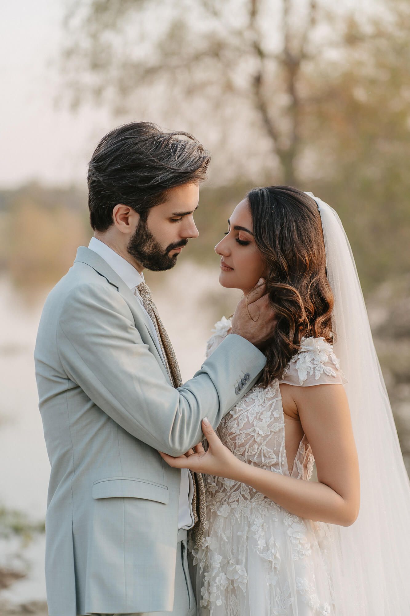 A romantic wedding photo of a couple sharing an intimate moment outdoors in soft natural lighting and elegant attire.