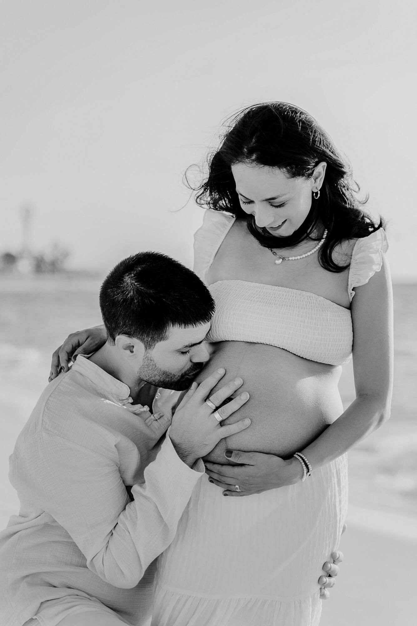 A tender black and white maternity photo series showing a parent kissing a pregnant belly in intimate moments.