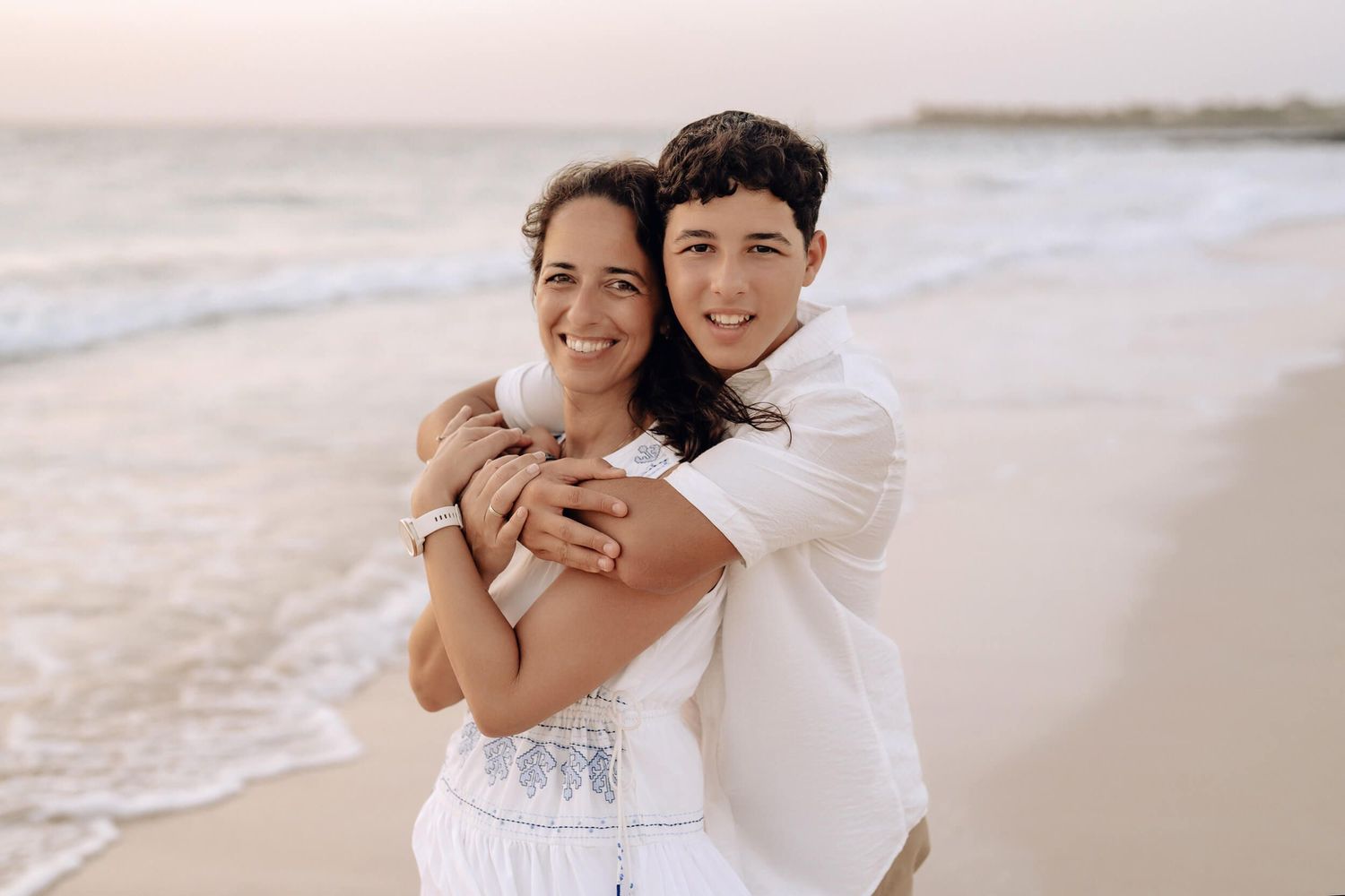 Casual beach portraits showing affectionate moments between two people in light colored clothing.