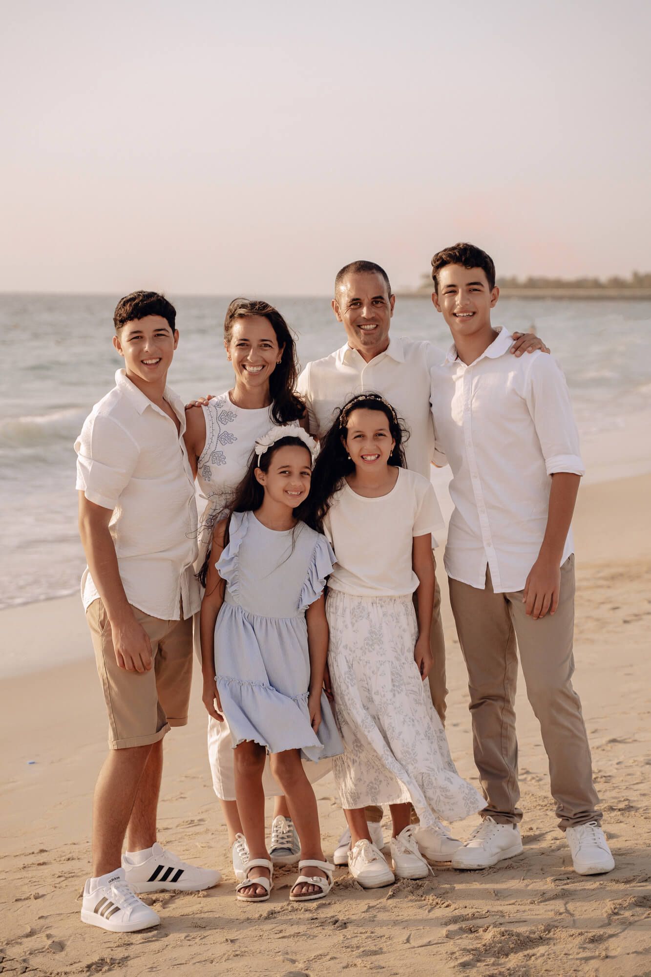Family of six poses for a casual portrait on the beach at sunset.