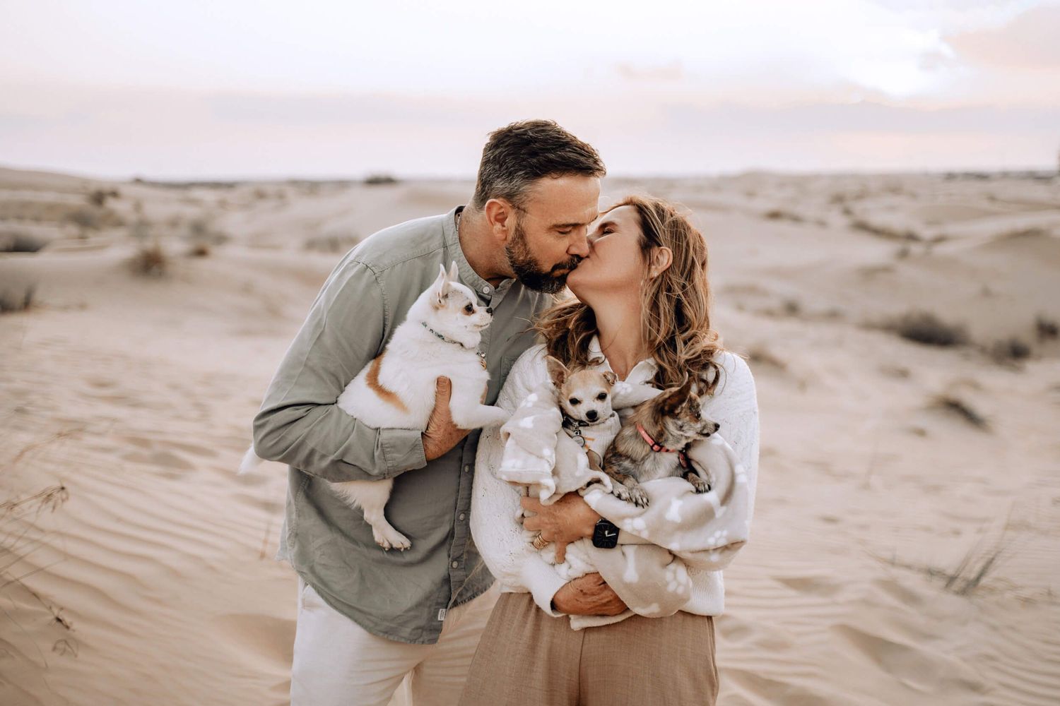 Black and white photo of a couple embracing their pet chihuahua in a desert setting.