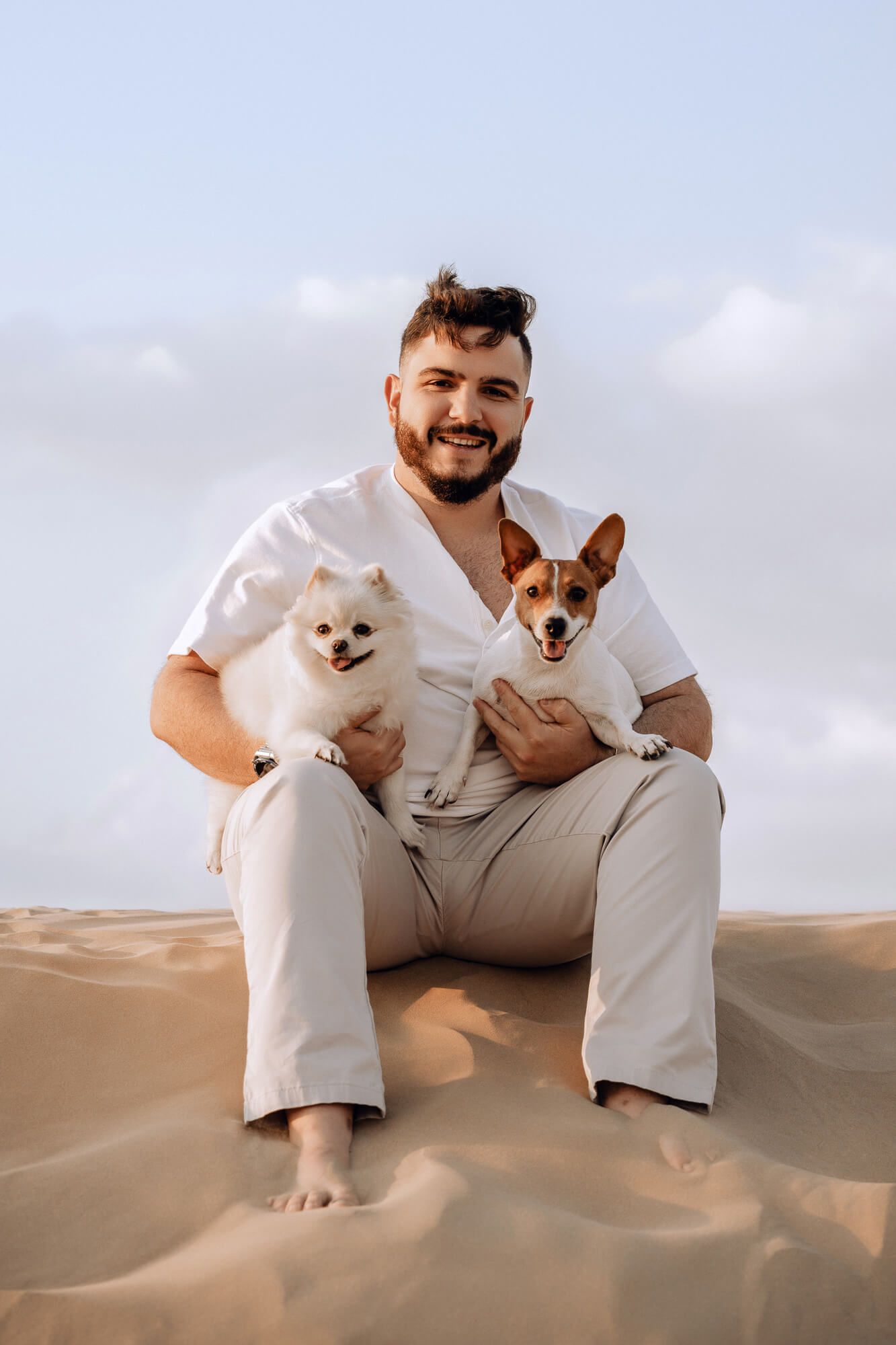 Two small dogs sitting on desert sand dunes during golden hour.