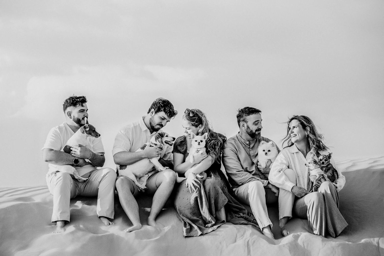Black and white portrait of group seated on sand dune with their small dogs.