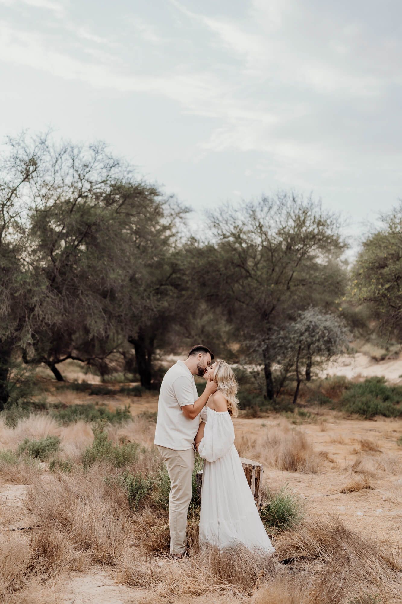 Ethereal pregnancy photoshoot in desert setting with couple in soft neutral colors.