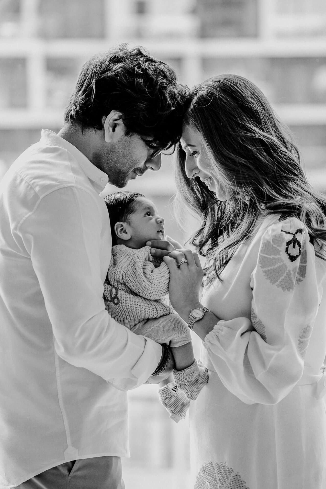 Black and white capture of parents sharing a close moment with their infant child.