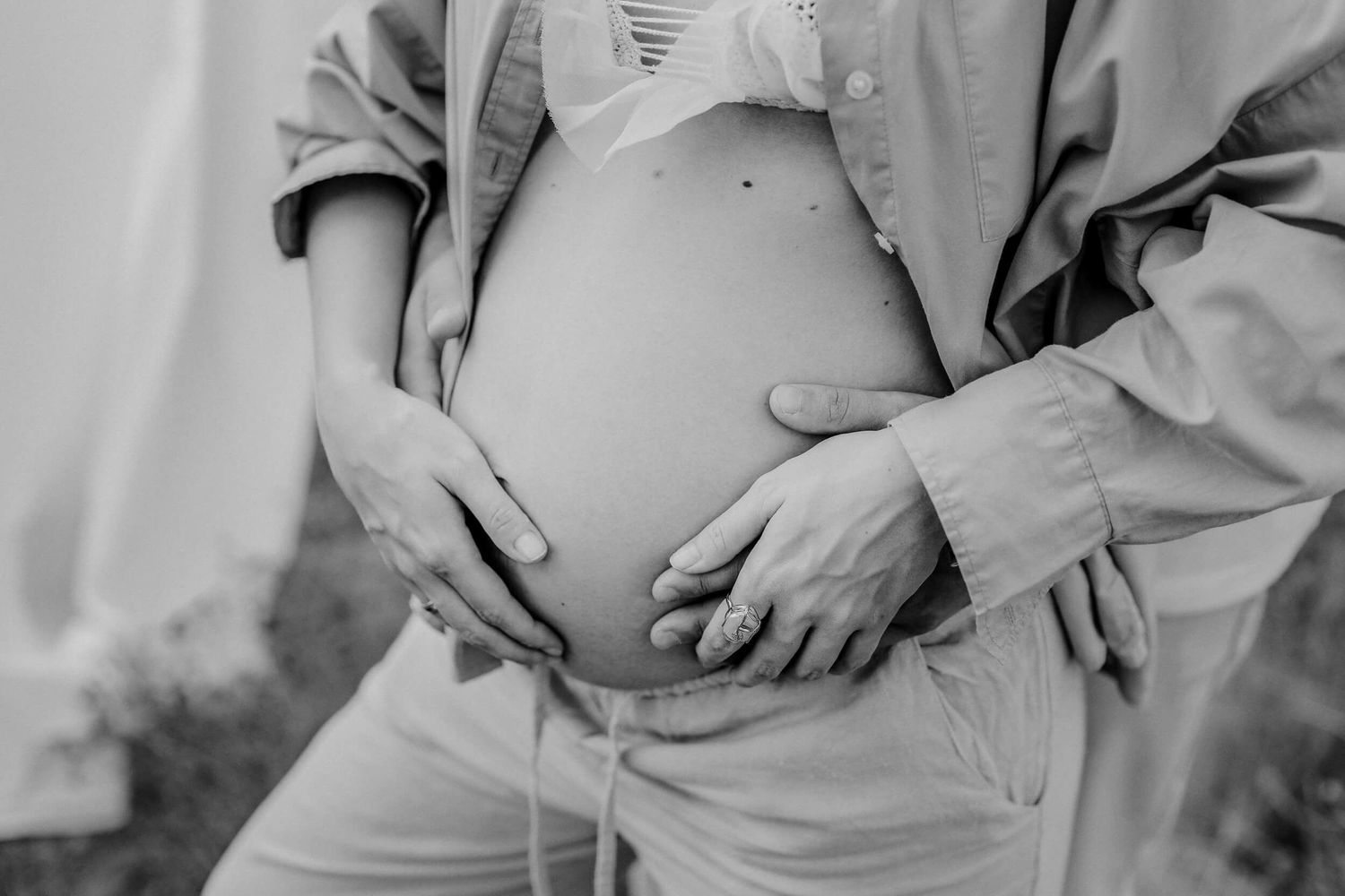 Black and white close-up of hands tenderly holding a pregnant belly.