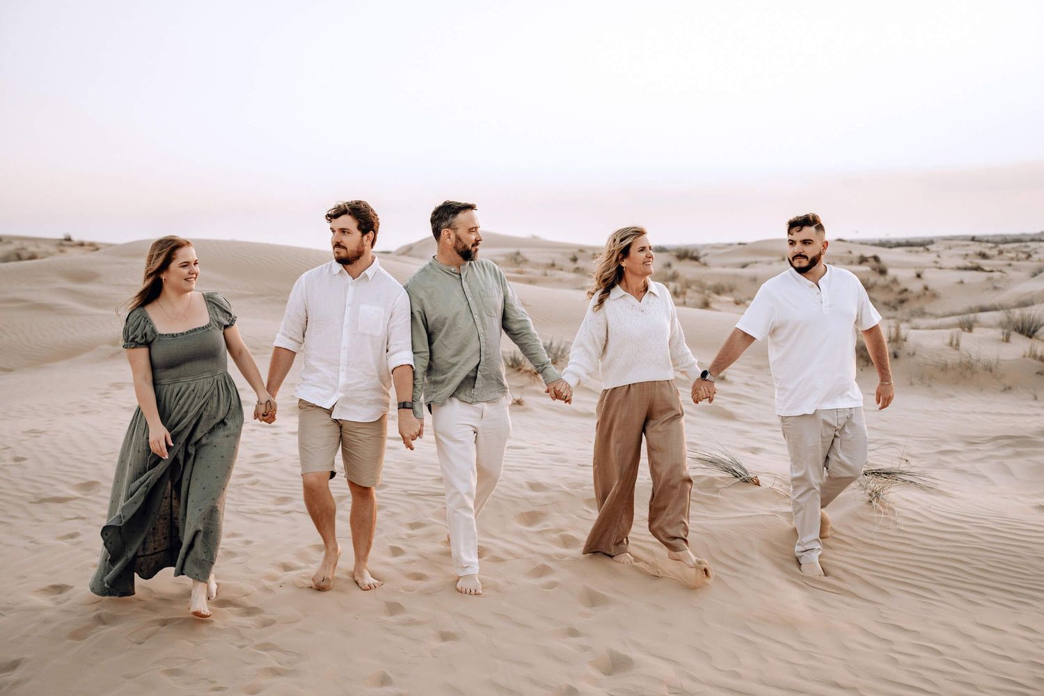 Group walking together through sand dunes at sunset wearing light colored clothing.