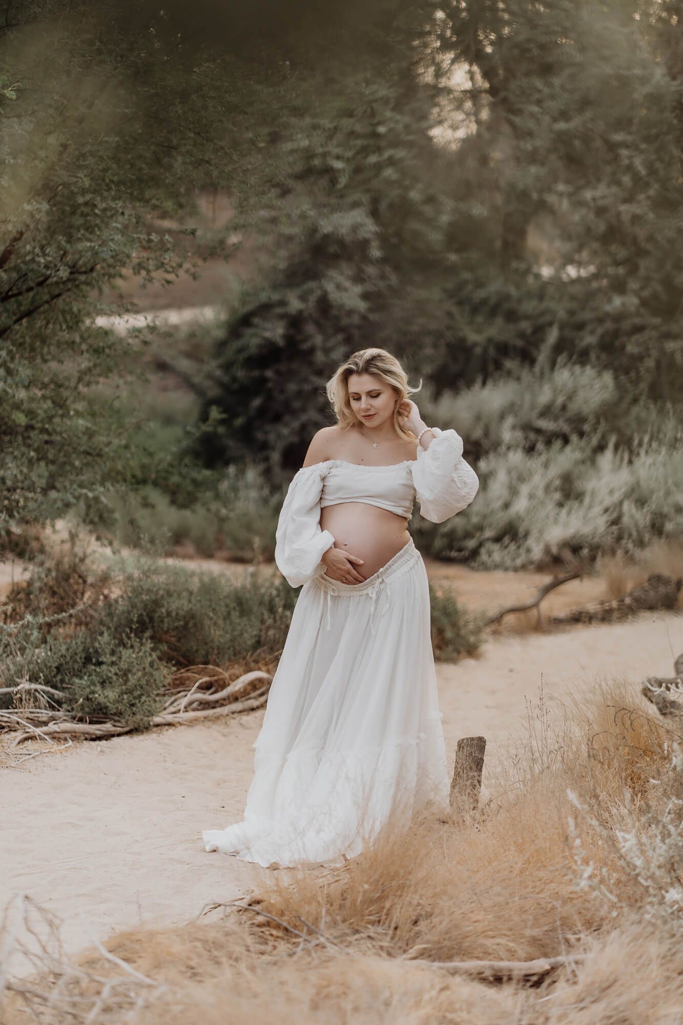 A maternity photoshoot featuring an ethereal white dress against golden natural scenery.