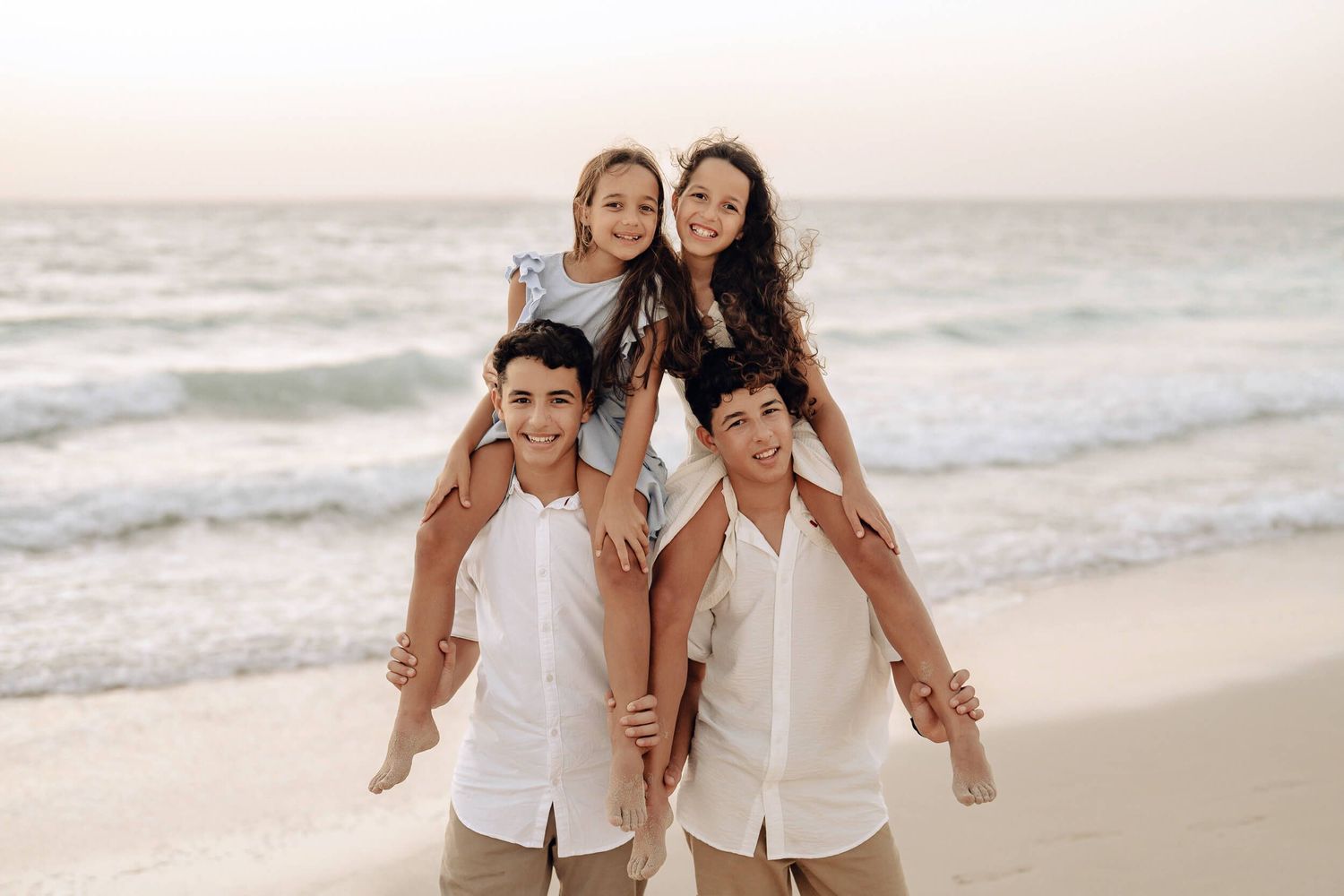 Two pairs on shoulders creating human towers while having fun on beach.