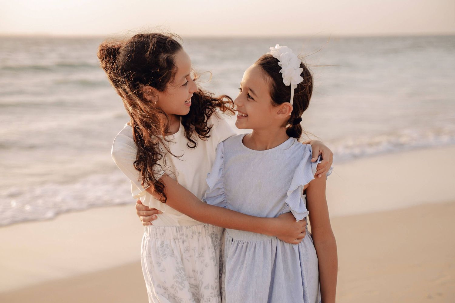 Sisters sharing a sweet moment together on the beach in pastel dresses.