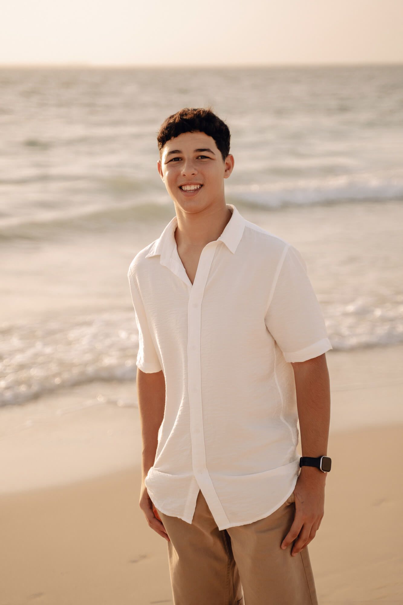 Portrait of person in white shirt and tan pants smiling on beach at sunset.