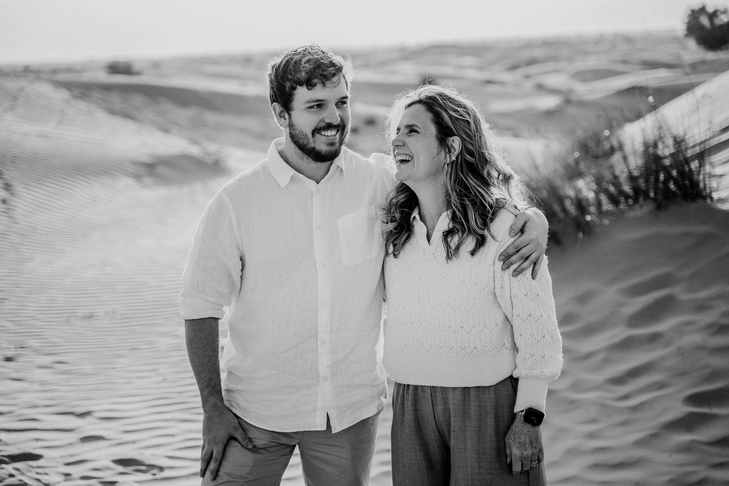 Monochrome desert portrait capturing genuine laughter against rolling dunes.