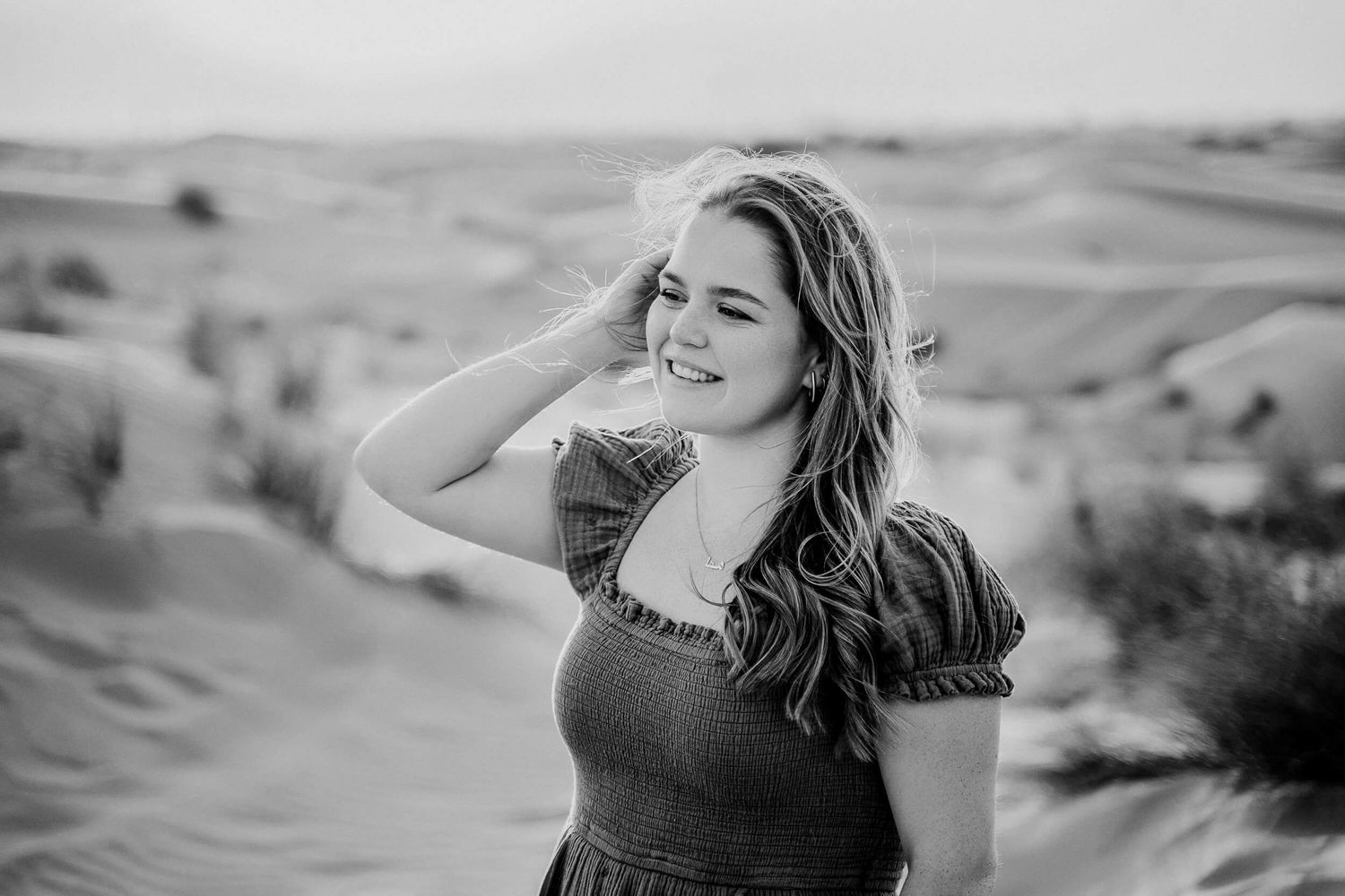 Black and white portrait of woman in dress smiling genuinely against desert background.