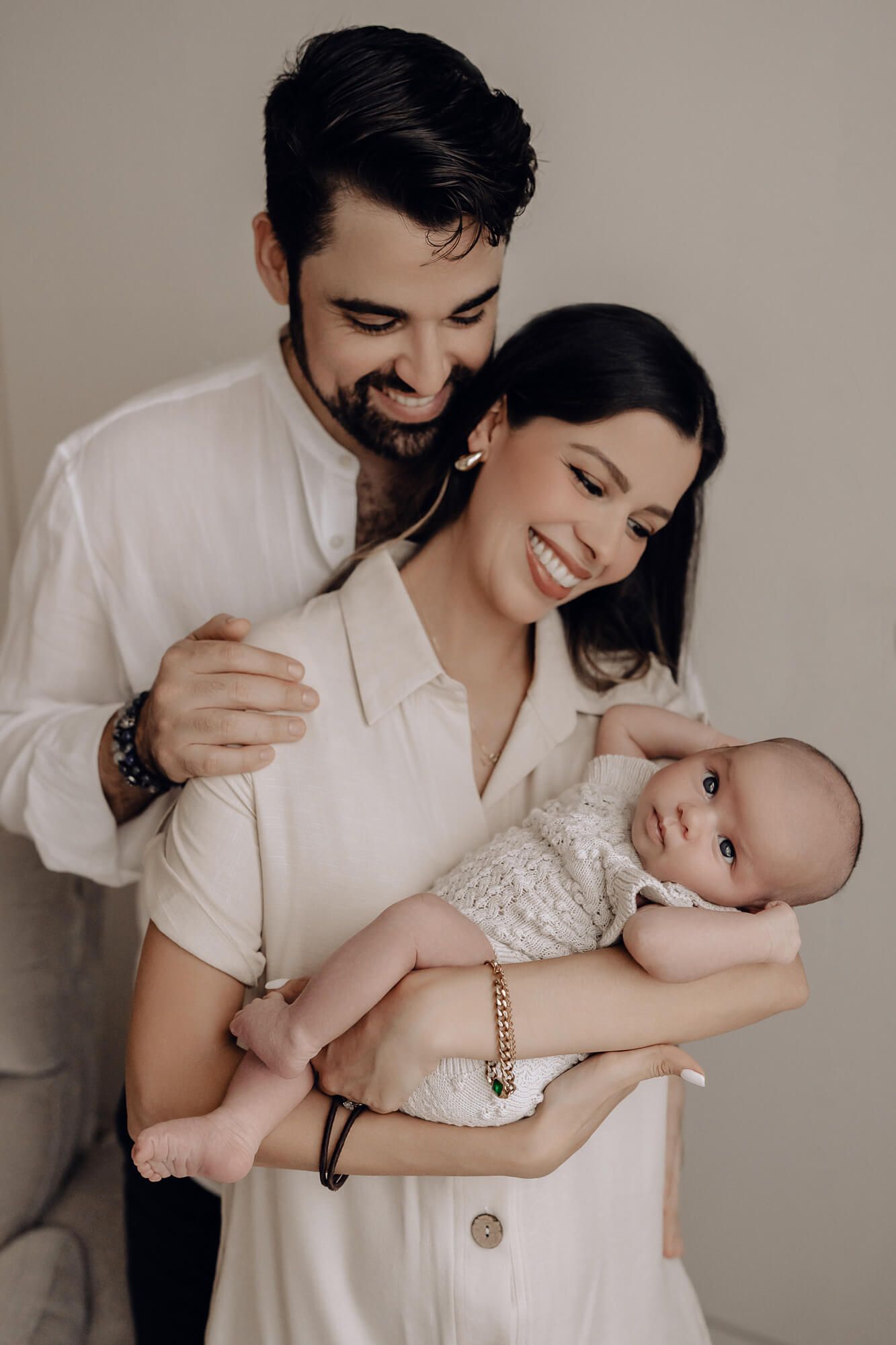 A family portrait in white clothing with a baby wearing a cream knit outfit.